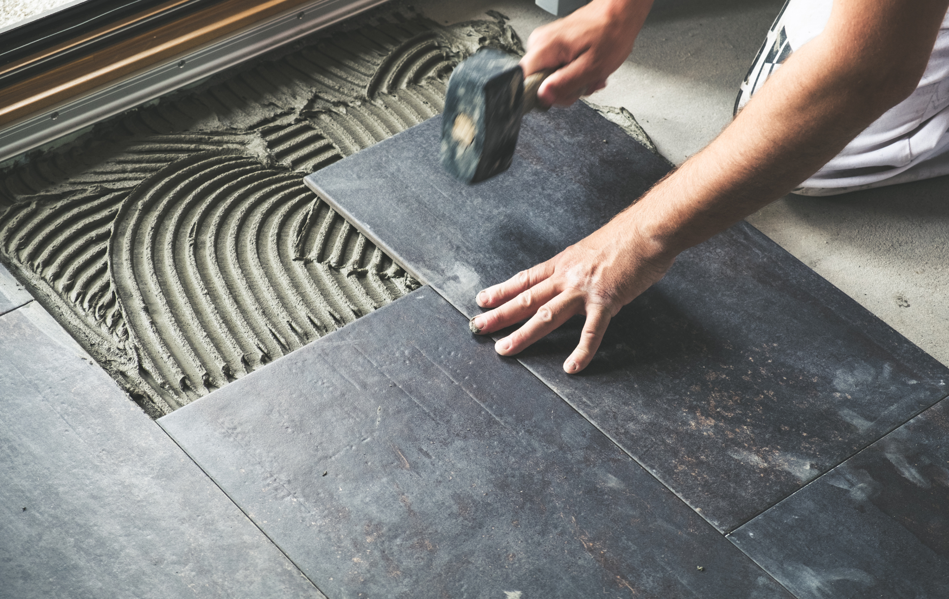 A person is laying tiles on the floor with a hammer.