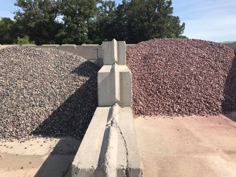 Two gravel piles, gray and red, split by a concrete divider on a sunlit lot