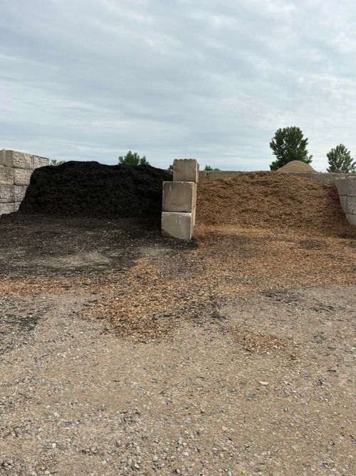 Piles of dark and tan gravel with a central concrete block in an outdoor yard under a cloudy sky