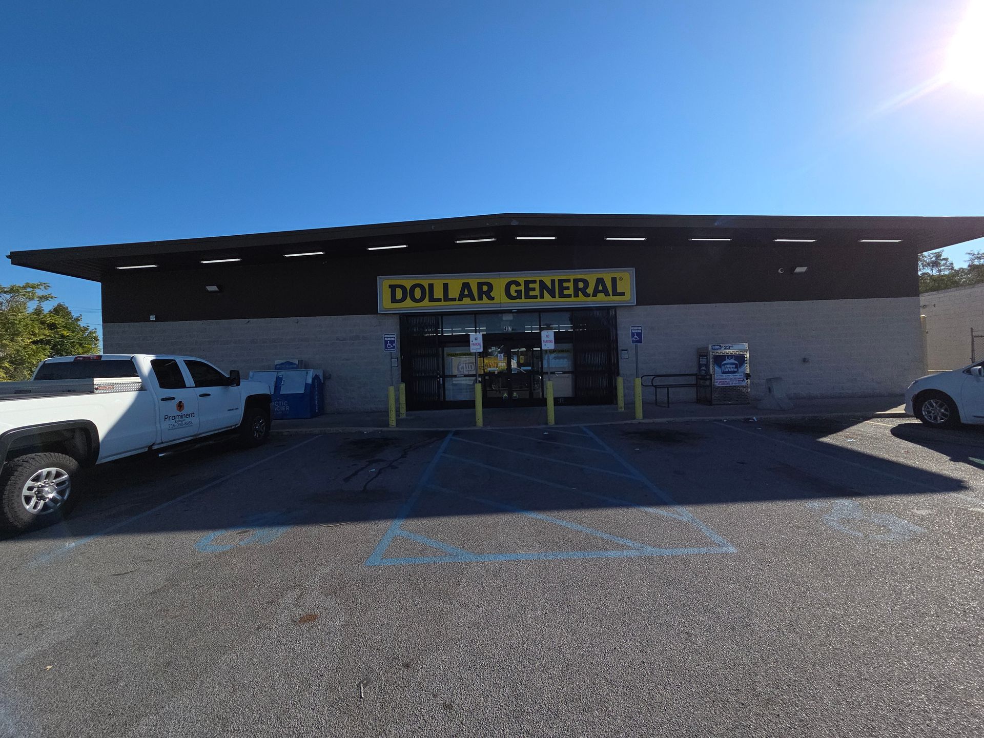 Dollar General store front with a blue sky, parked vehicles, and a yellow sign.