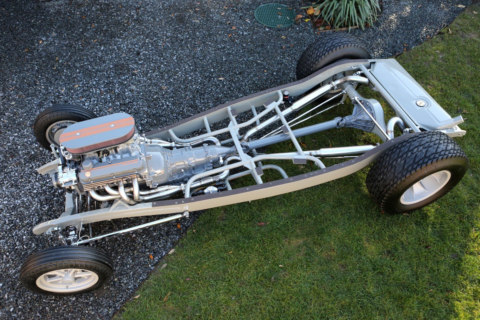 Exposed sand rail dune buggy chassis with orange engine, parked on grass and gravel