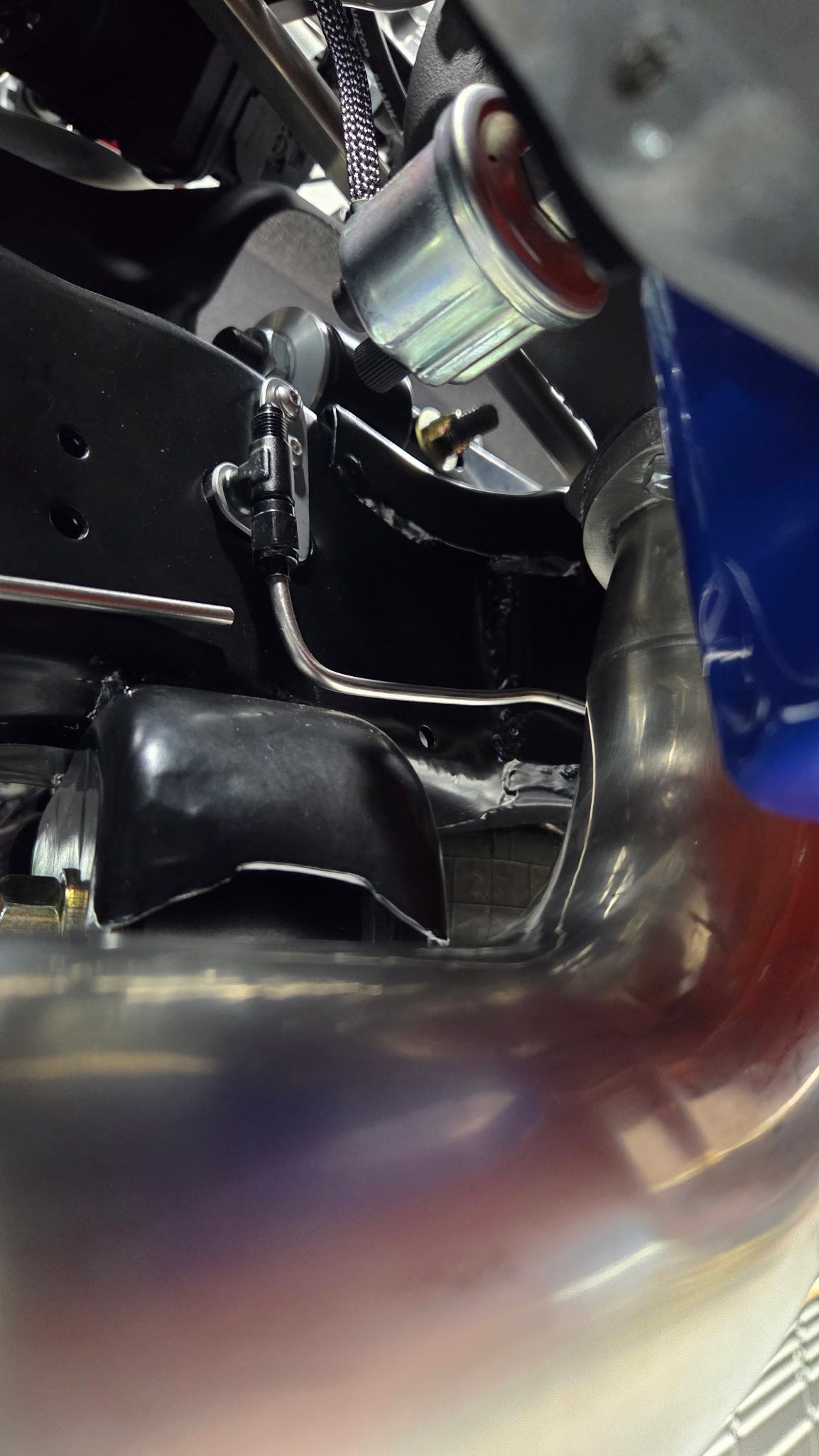 Close-up of a metallic mechanical assembly with black parts, silver fittings, and a blue hose.