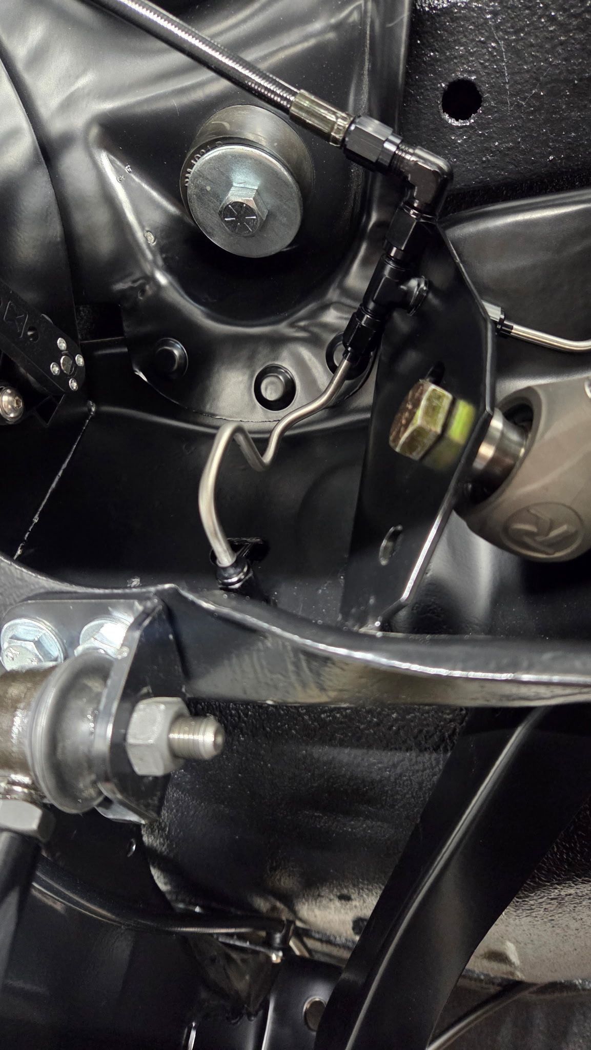Close-up of black motorcycle engine components with bolts, hoses, and a small fluid reservoir.