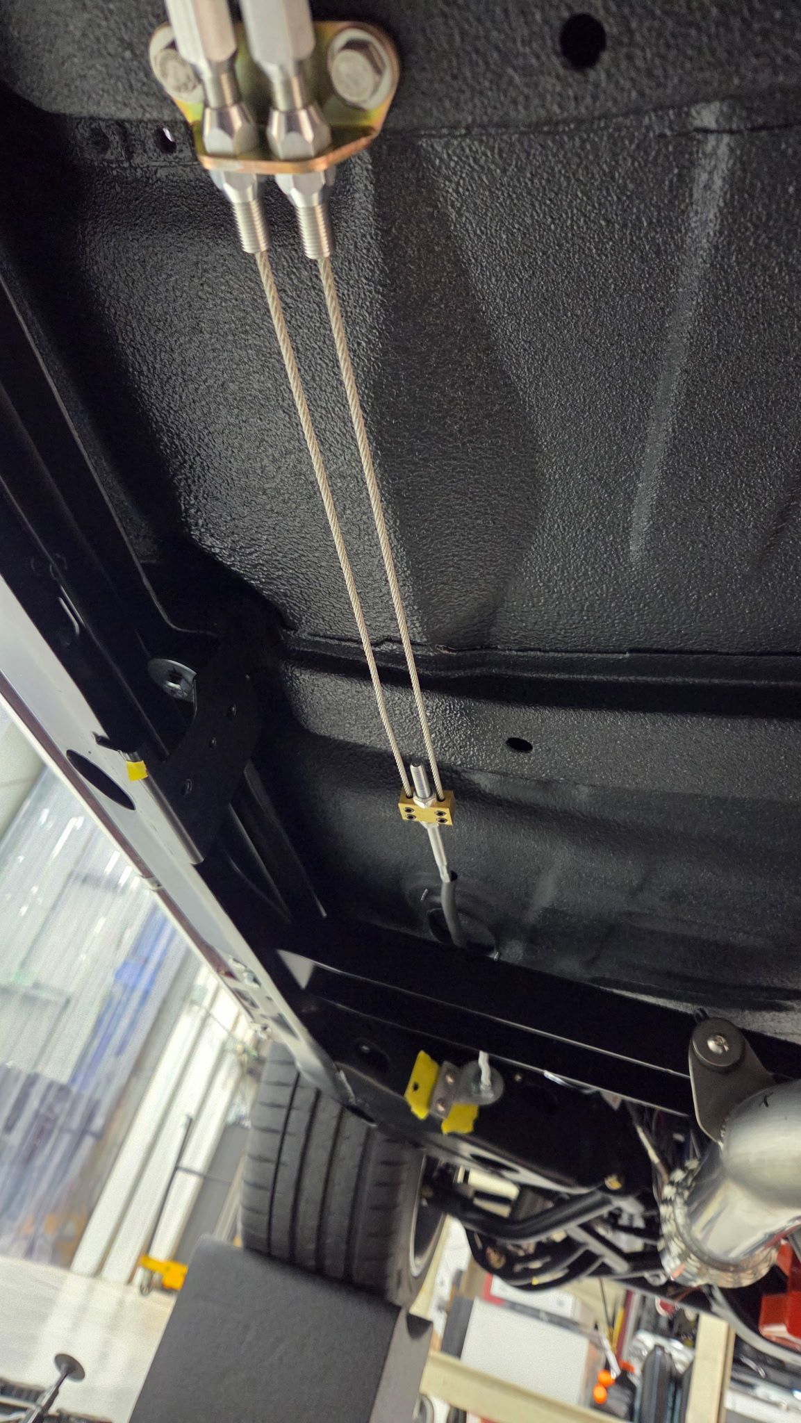 Undercarriage of a vehicle on a lift, showing exposed metal frame and hanging hoses.