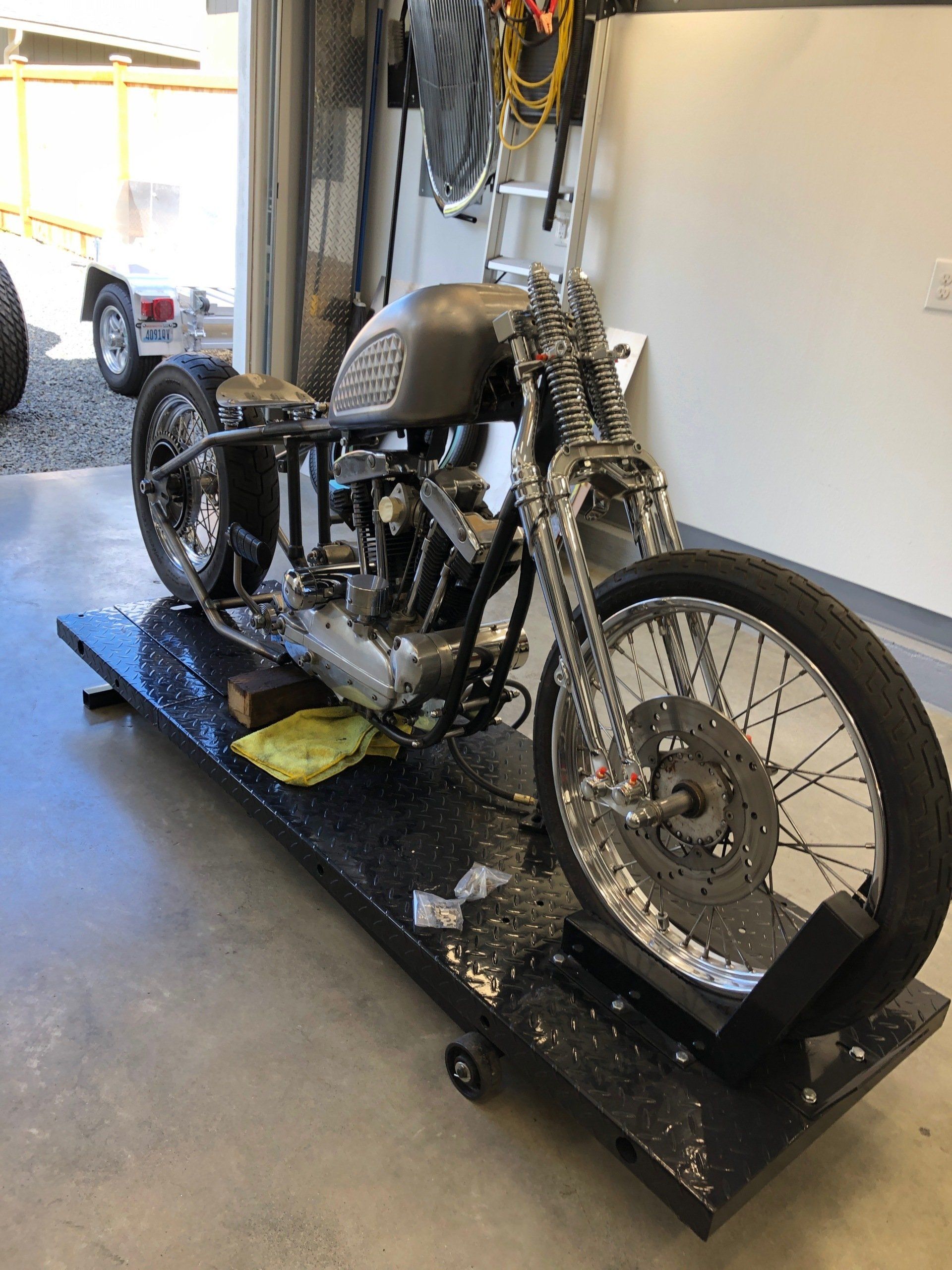 Motorcycle strapped on a black transport stand in a garage, with a wheel chock and tie-downs attached