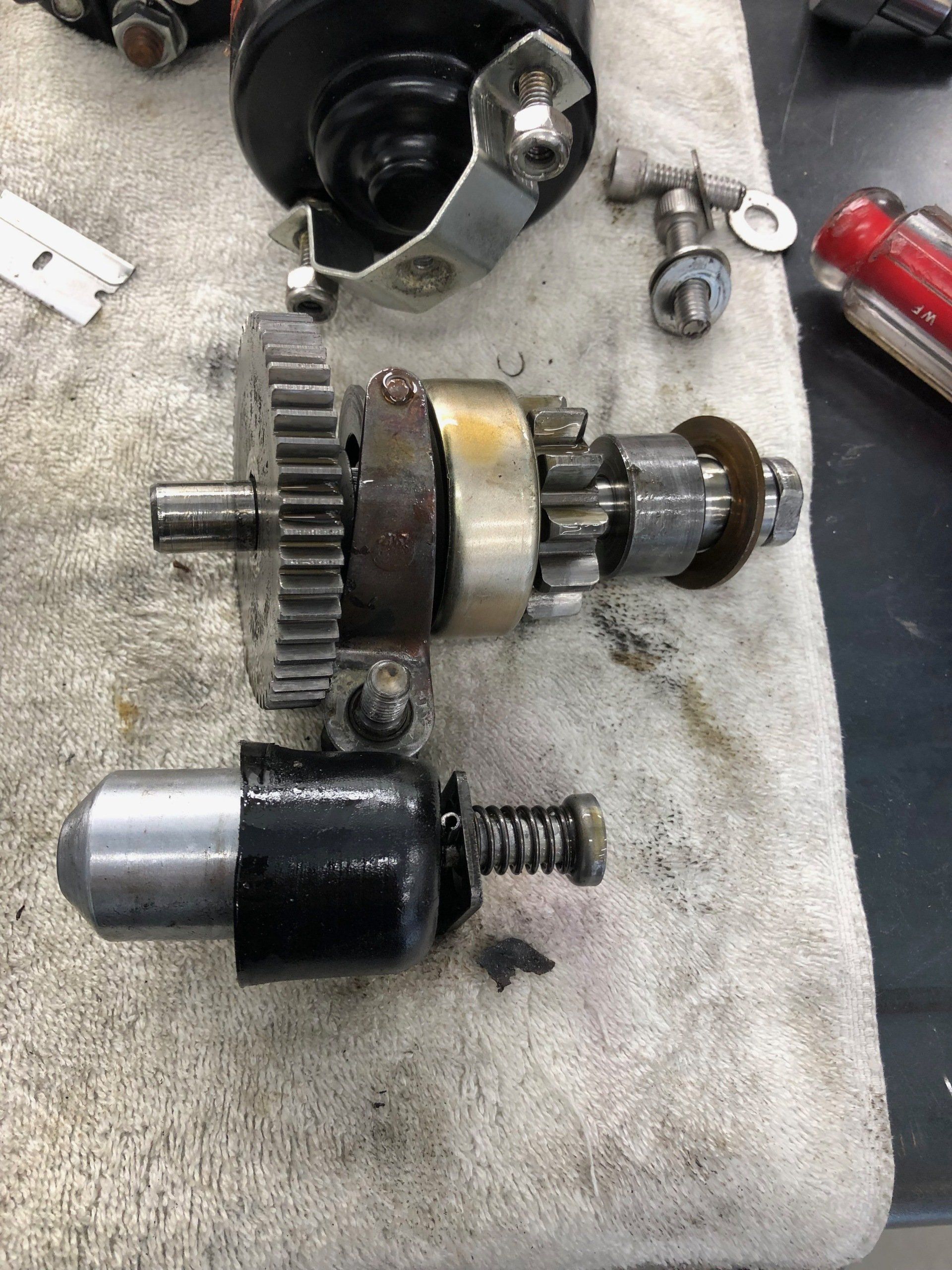 Two metal mechanical parts on a workshop towel, including a gear shaft and black-and-silver cylinder.