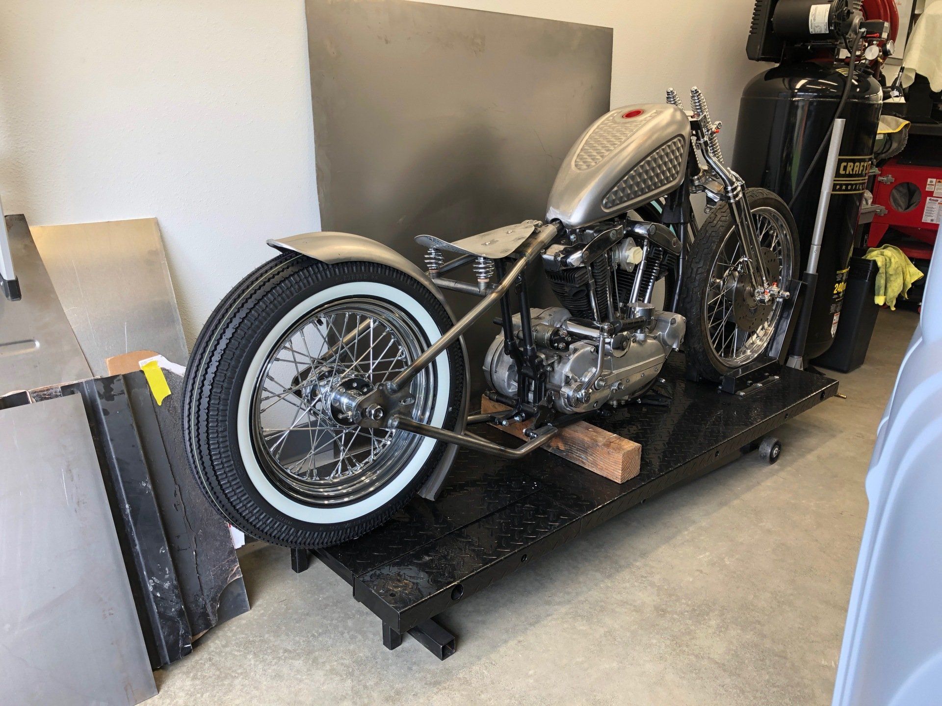 Custom motorcycle on a black lift in a garage, with chrome engine and whitewall tires.
