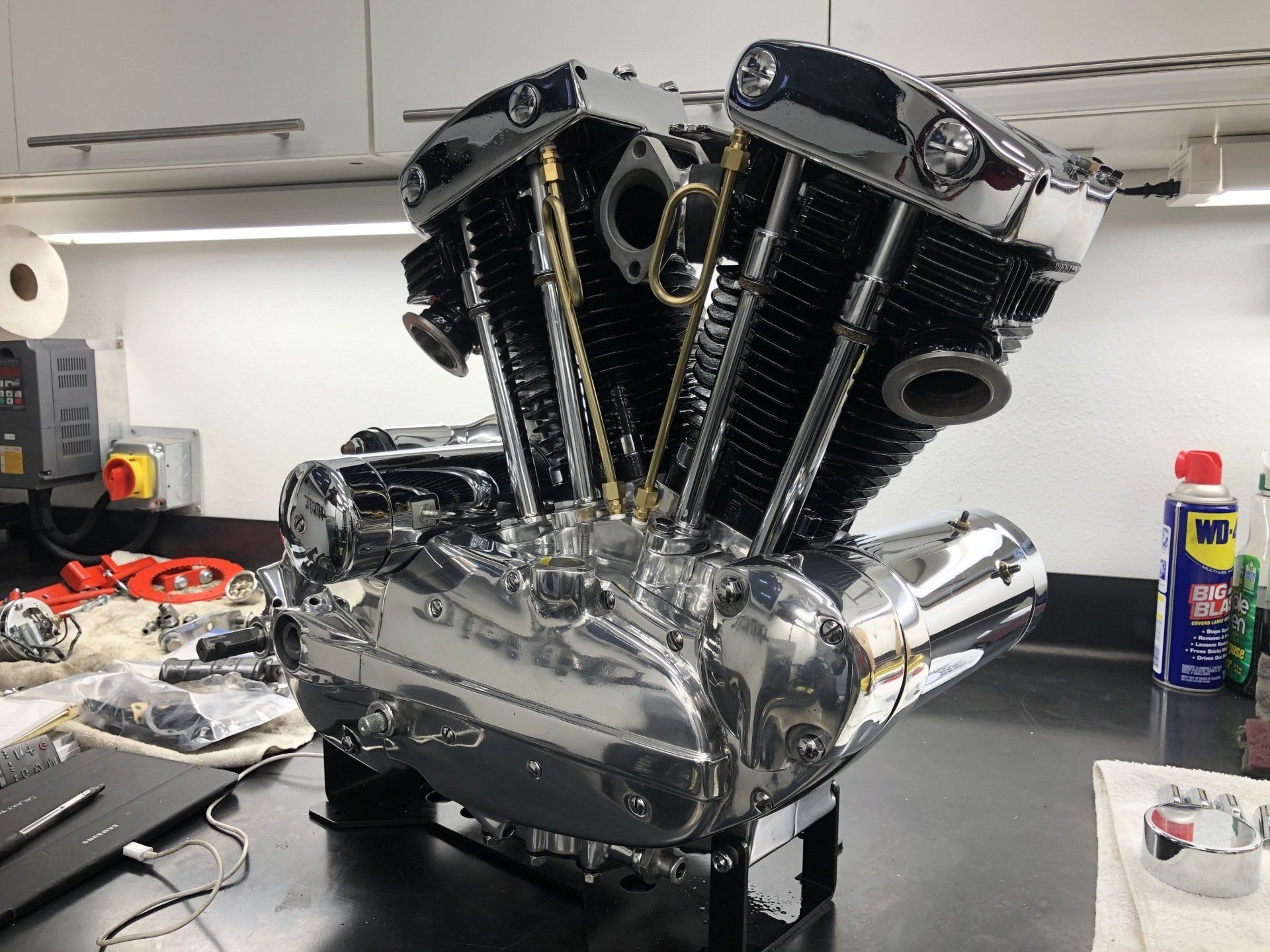 Chrome V8 engine model on a workbench, with black valve covers and polished intake pipes.