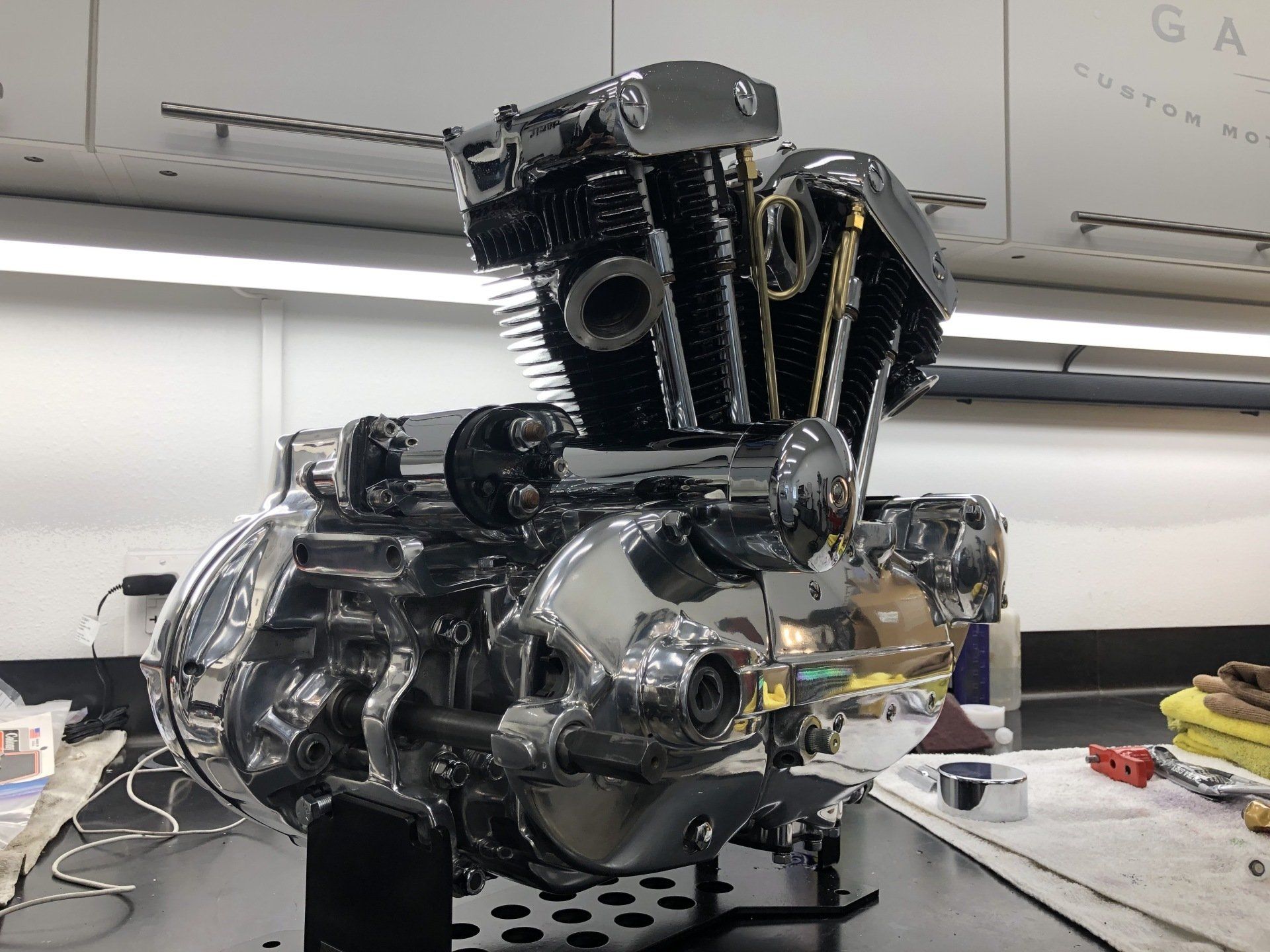 Shiny black-and-chrome motorcycle engine on a workbench in a workshop, with tools nearby