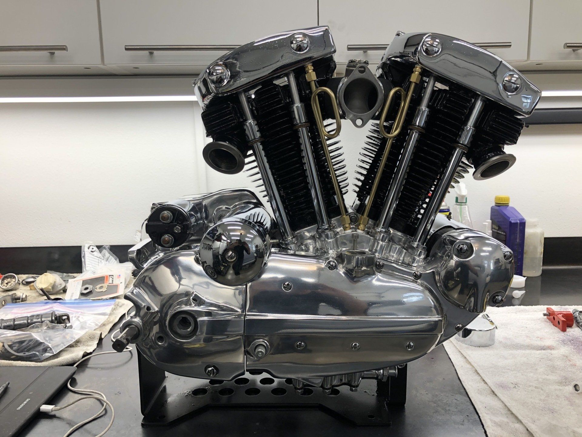 Chrome V-twin motorcycle engine on a workbench in a garage, with black cylinder fins and polished metal covers