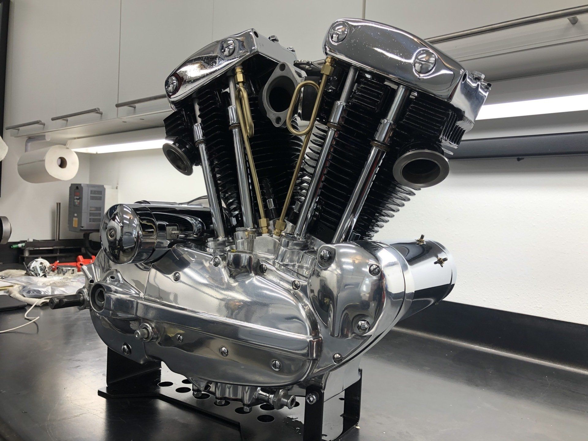 Chrome V-twin engine on a workbench in a workshop, with polished metal and black cylinder fins.