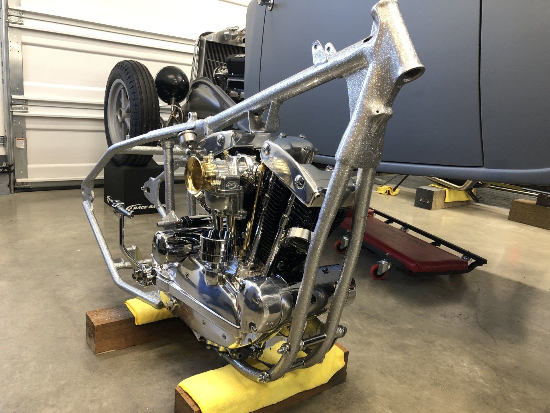 Bare motorcycle frame on yellow supports in a garage, with exposed engine and wheels attached