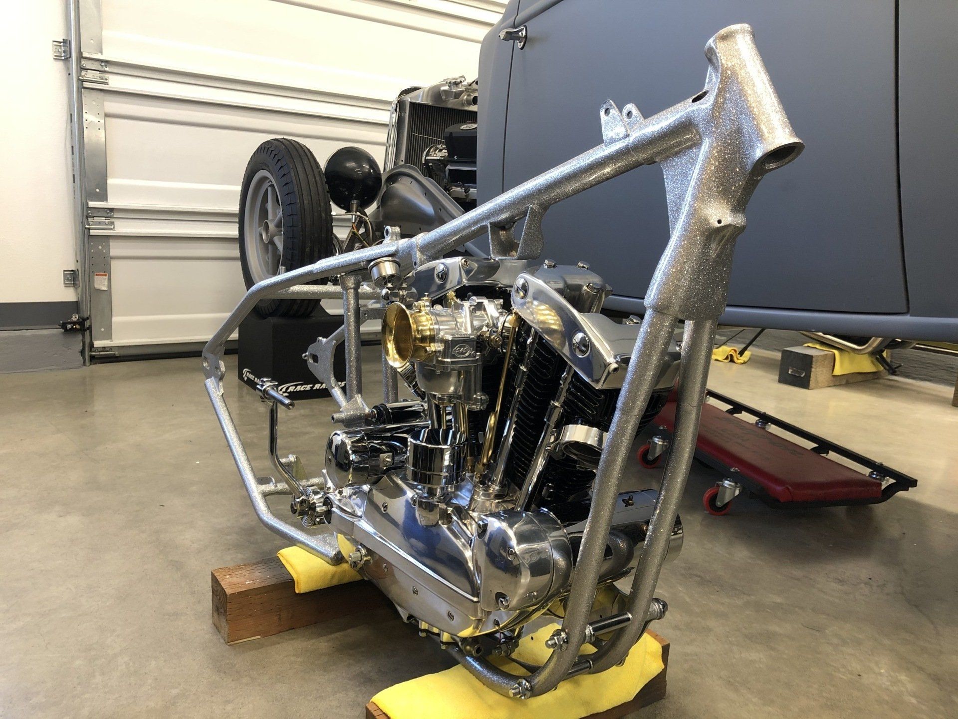 Custom motorcycle frame and engine assembly in a garage, propped on wooden blocks.