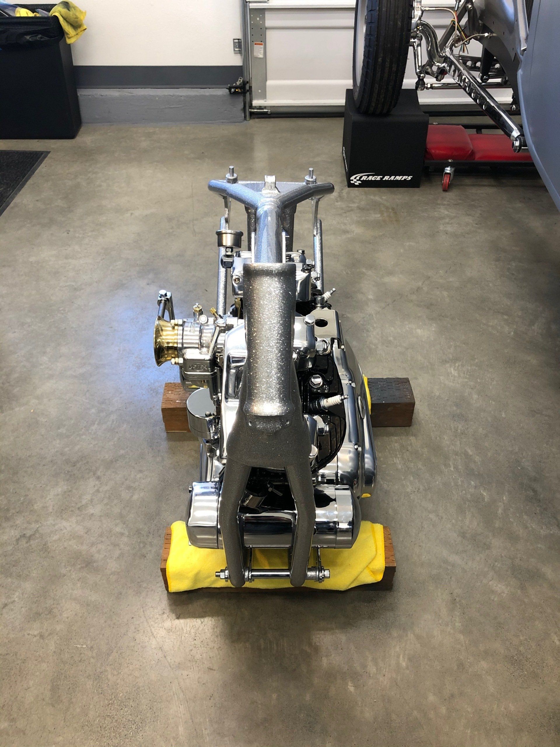 Silver mechanical equipment on a shop floor, centered on a yellow base with wheels and tools in the background