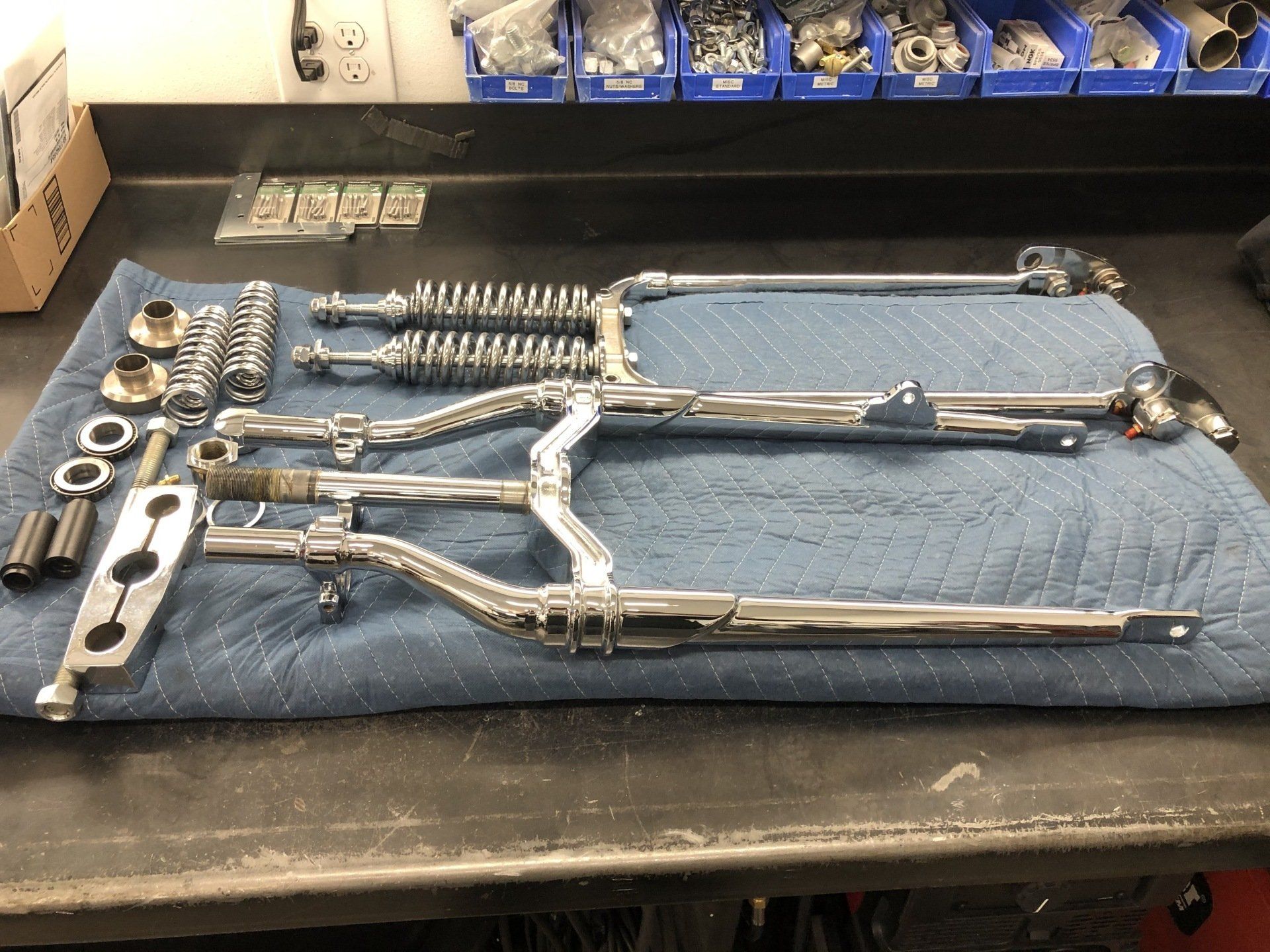 Assorted metal tools and parts laid out on a workbench under a blue mat, with long-handled pliers in the center