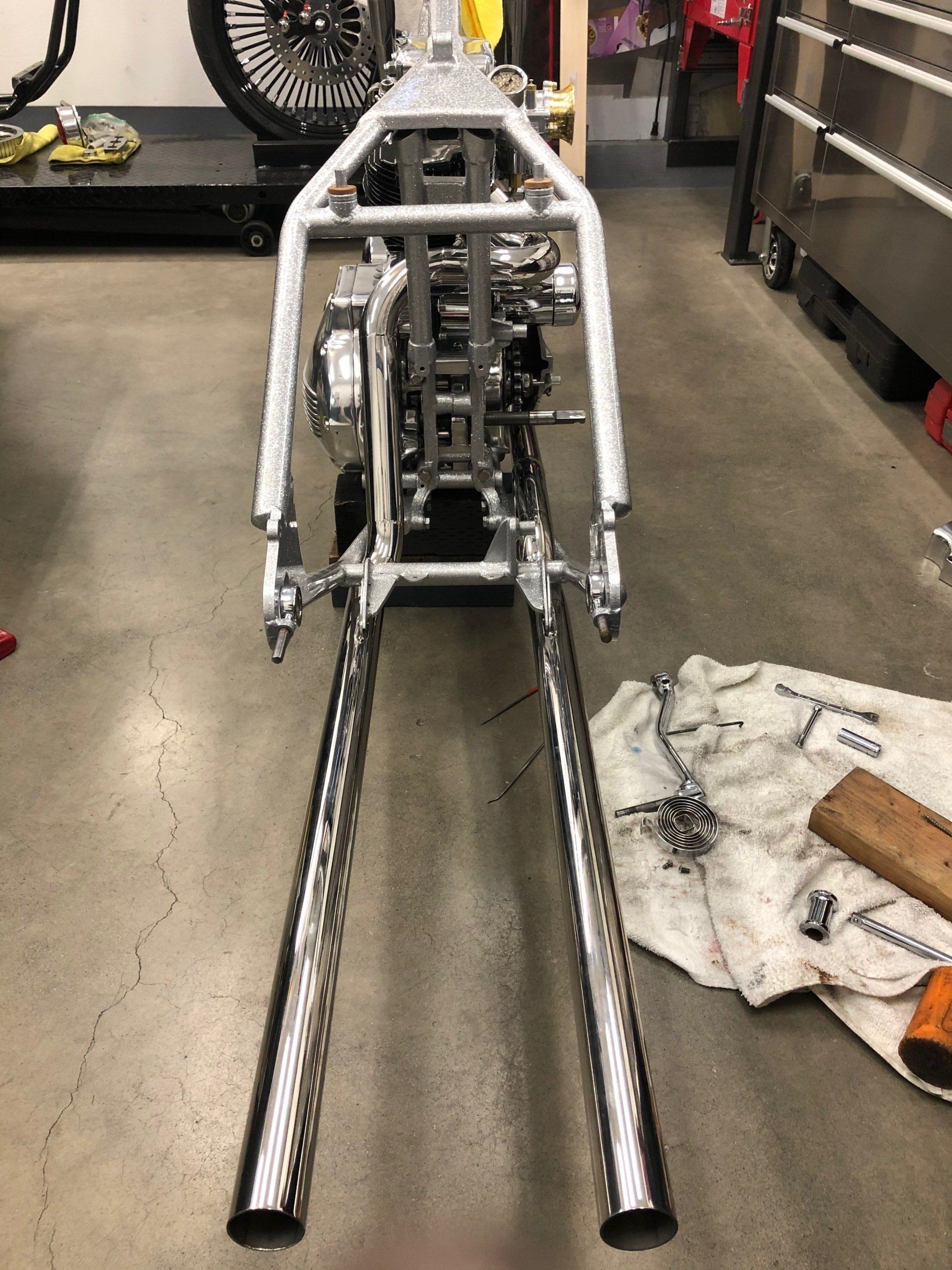 Bare metal custom motorcycle frame with long fork tubes in a garage workshop