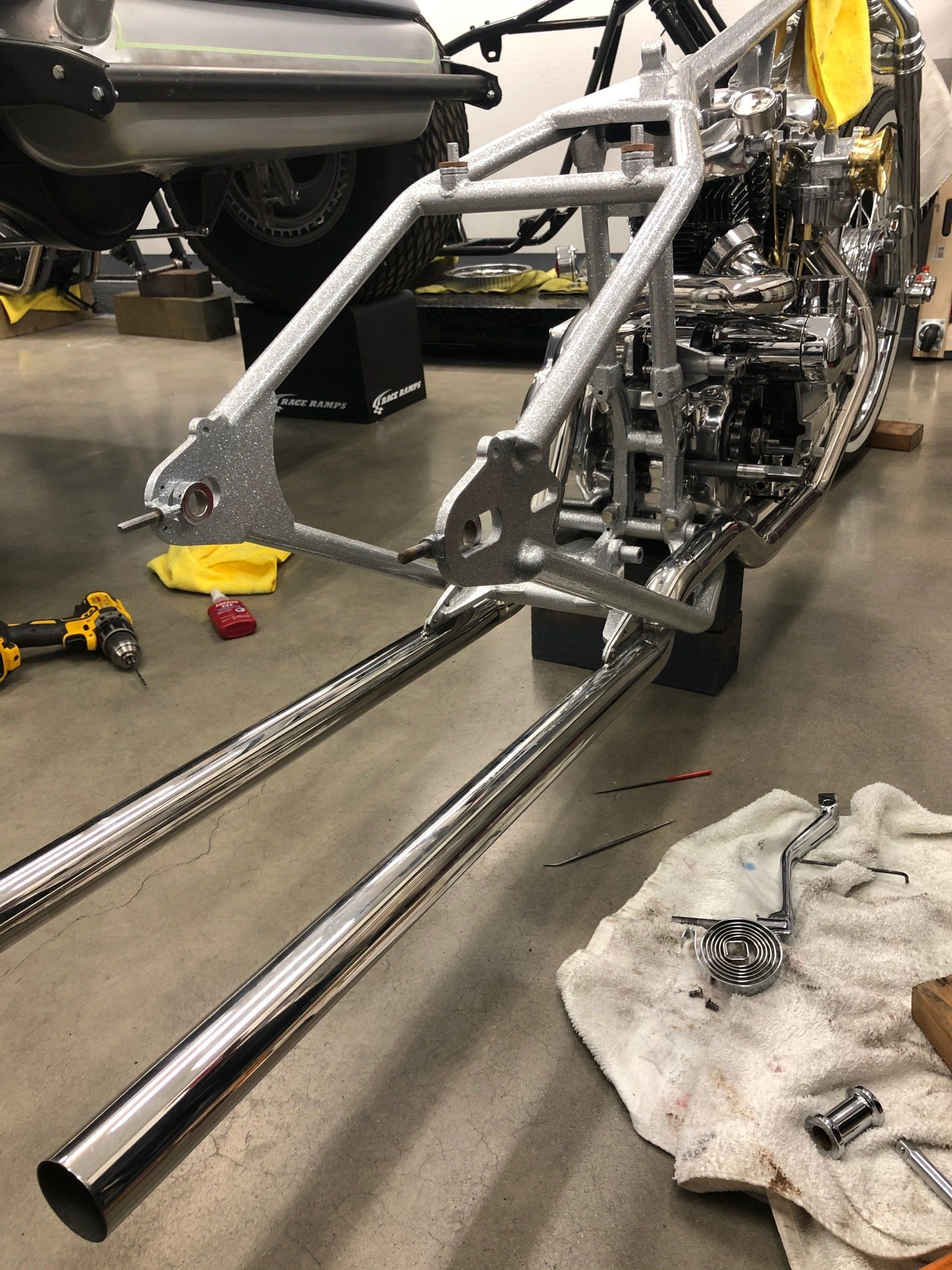 Custom metal vehicle chassis frame in a workshop, with polished front rails and tools on the floor.
