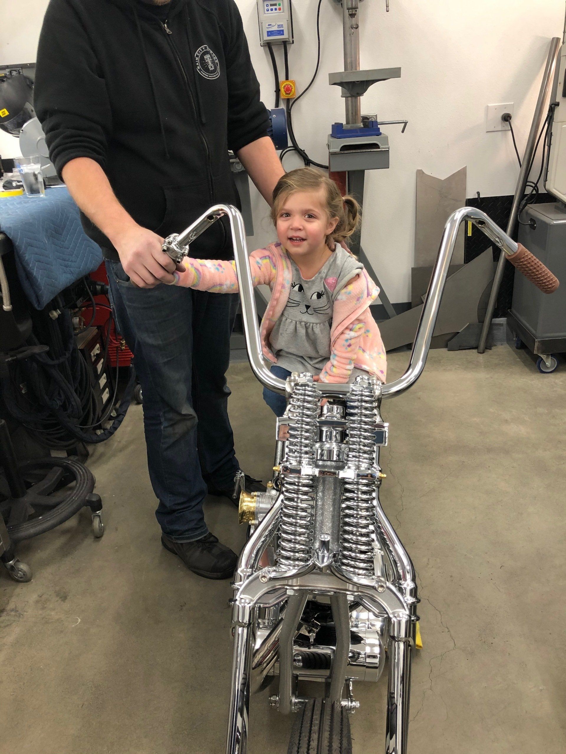 Child in a seated mobility device smiling while holding an adult’s hand in a workshop setting