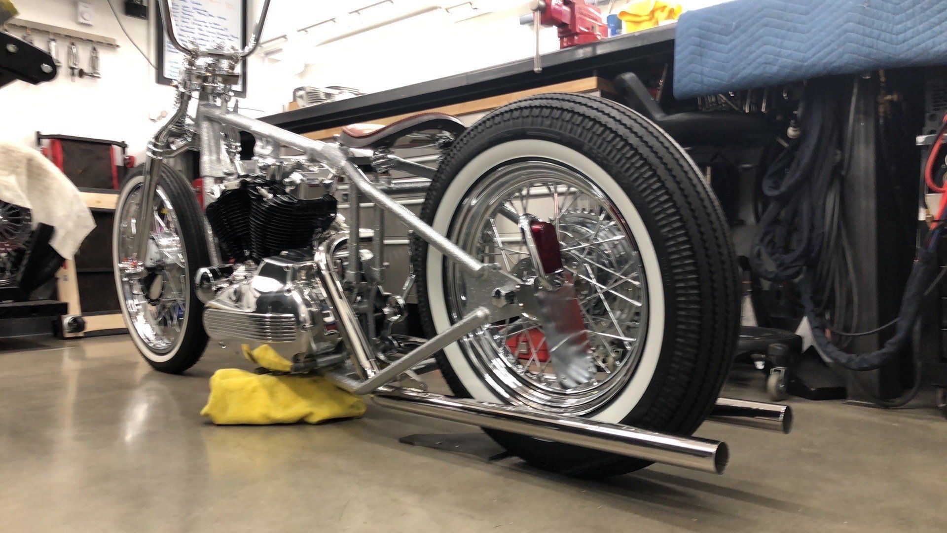 Low-angle view of a custom black hot rod with chrome wheels in a garage, supported by wheel dollies.