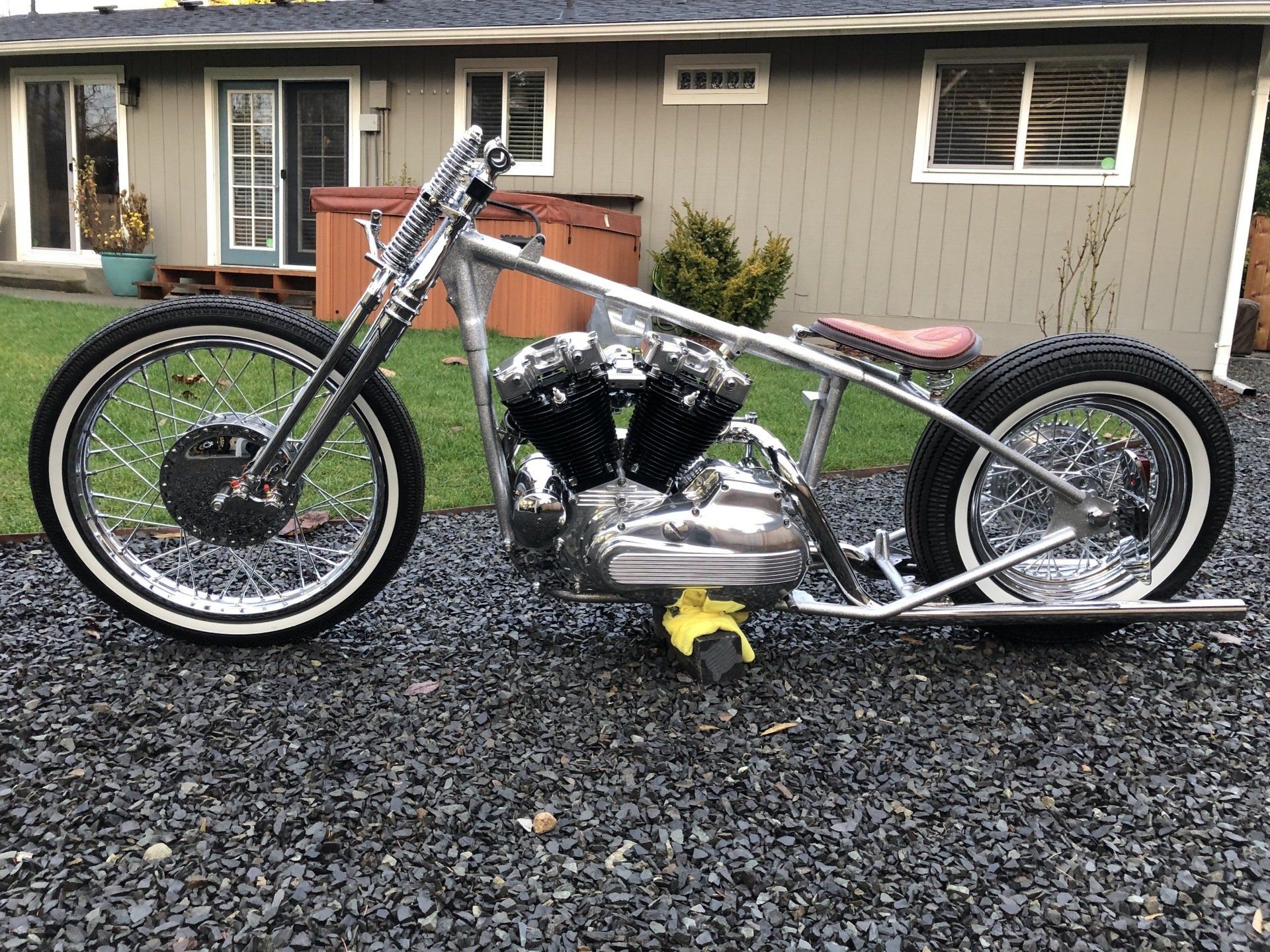Custom silver chopper motorcycle parked on gravel in front of a house