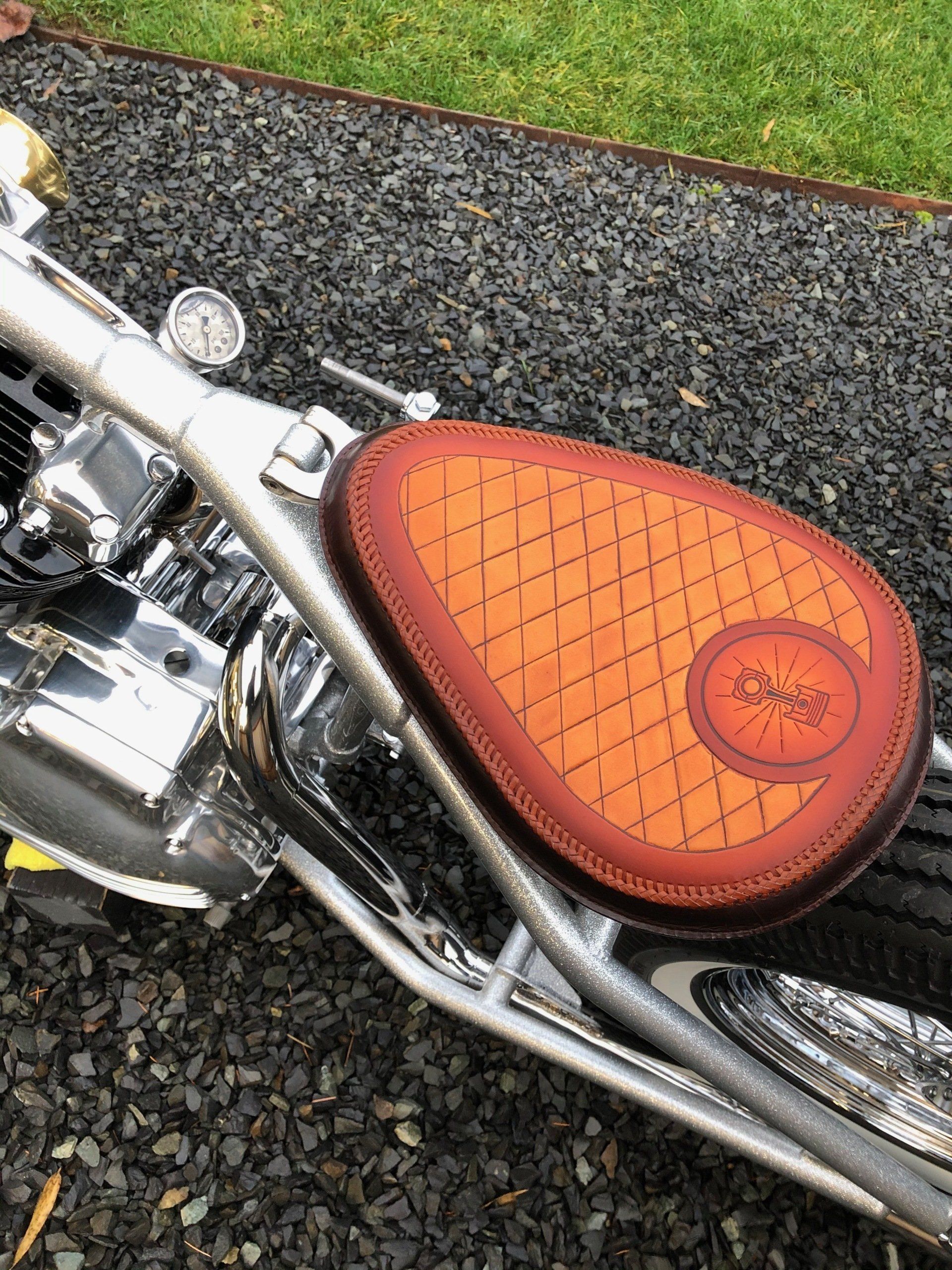 Orange leather motorcycle seat with diamond stitching on a chrome bike, parked on gravel