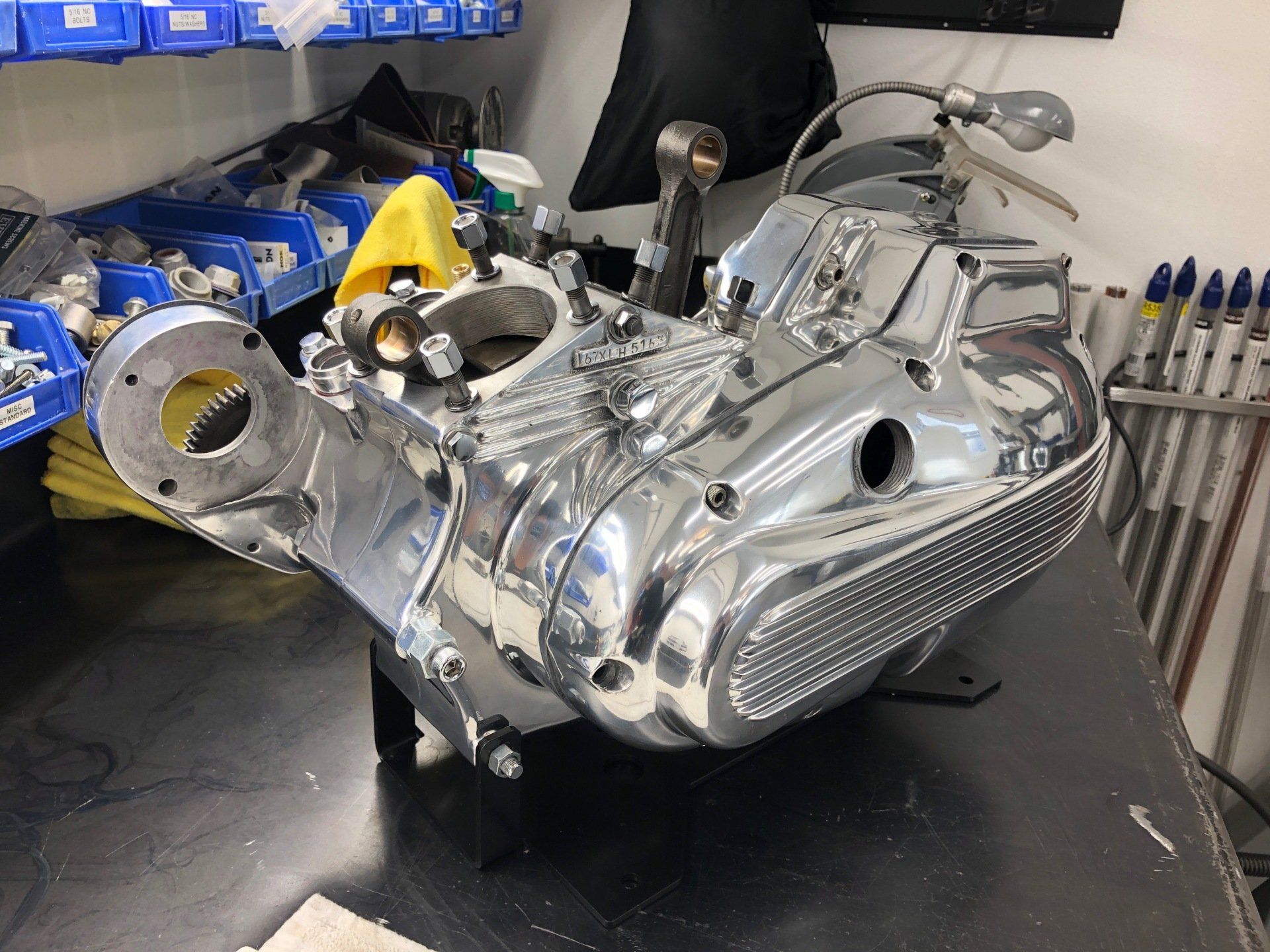 Shiny motorcycle engine assembly on a workbench in a workshop, with tools and parts nearby