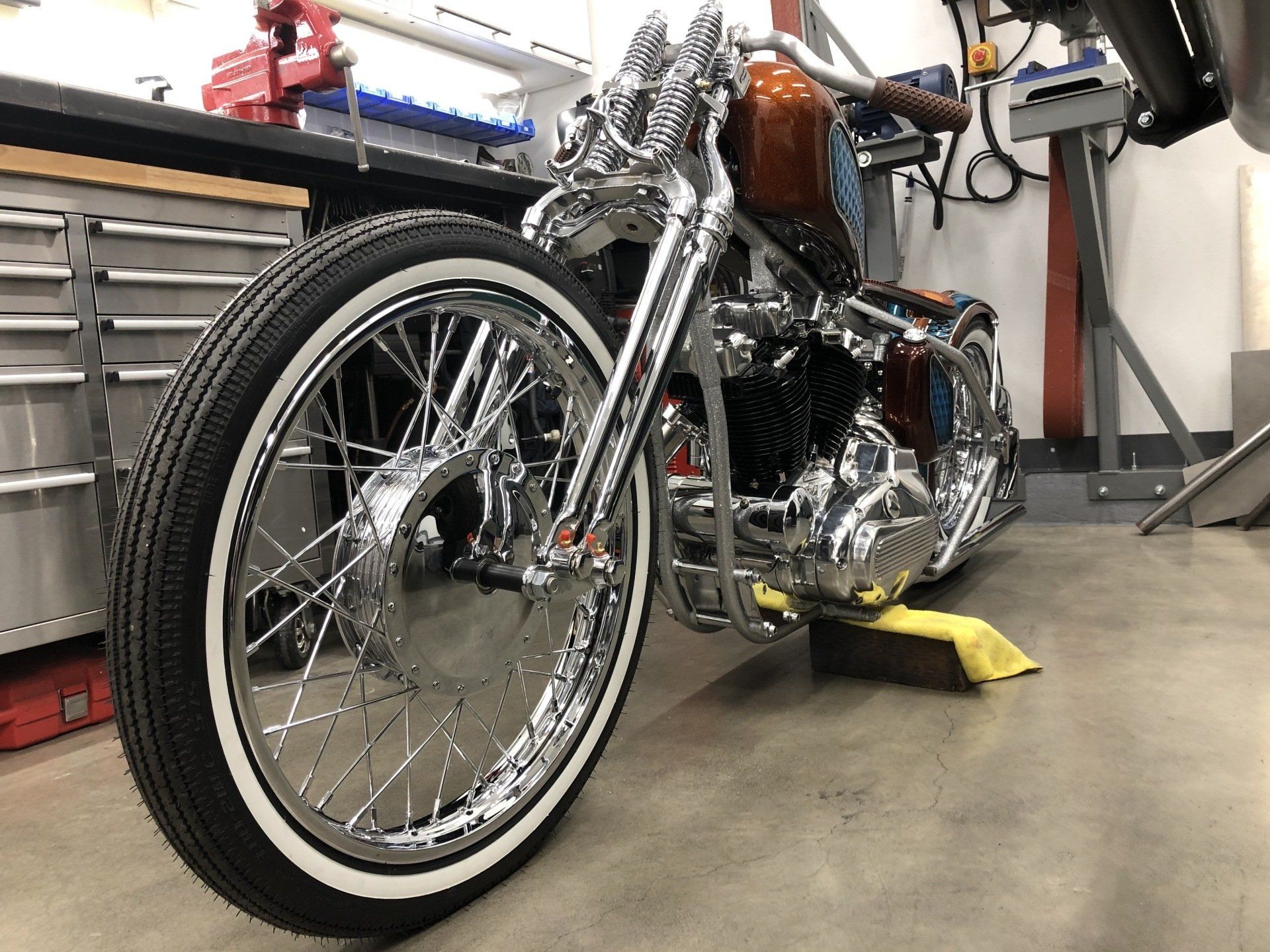 Custom chrome motorcycle in a garage, with a yellow wheel chock and workshop tools in the background