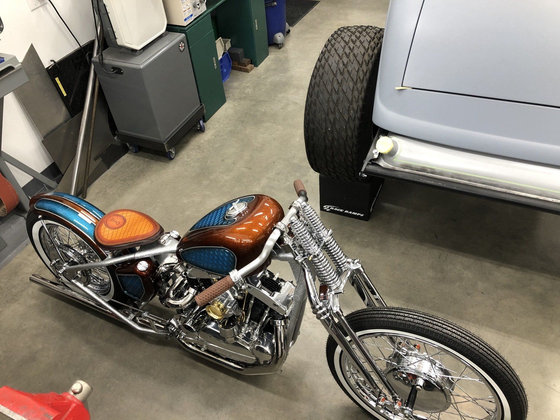 Custom chopper motorcycle with orange seats parked in a garage beside a light gray car