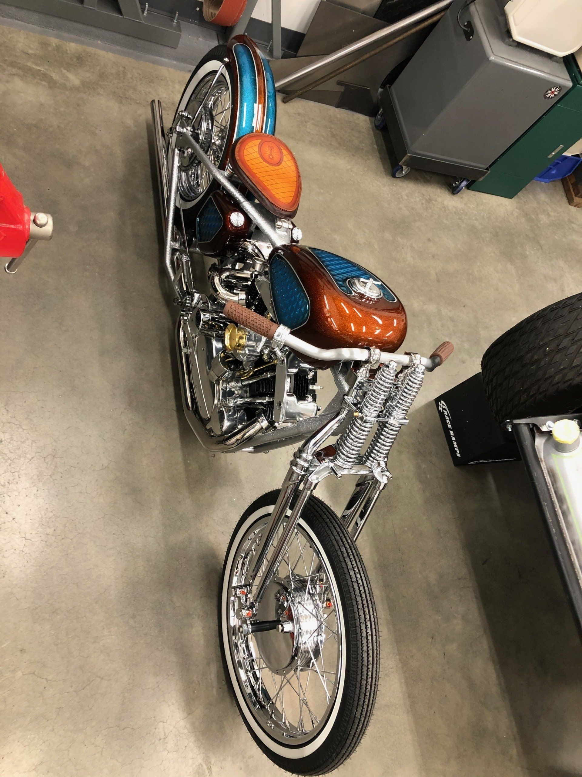 Custom orange-and-blue motorcycle with chrome accents in a garage or workshop.
