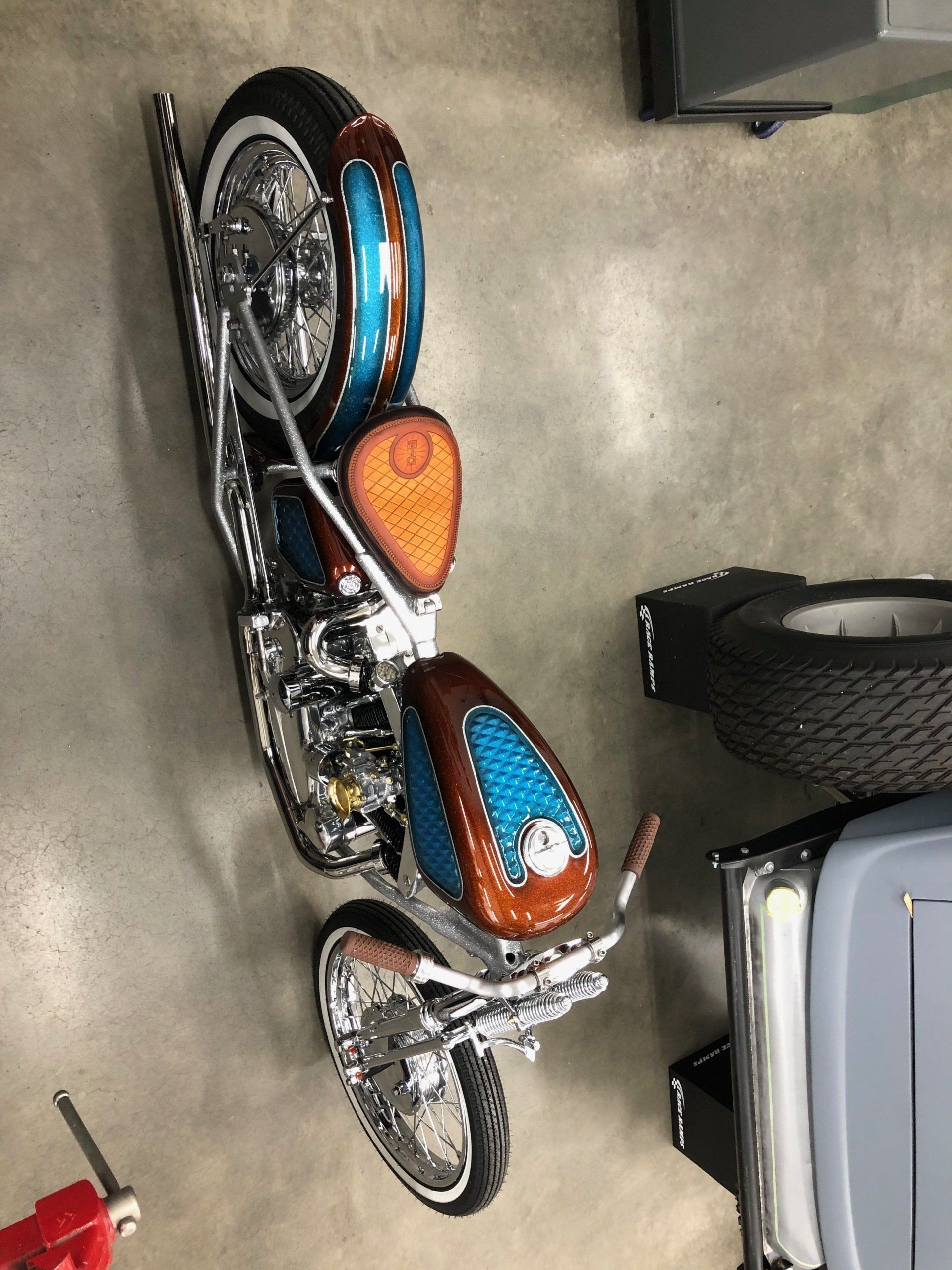 Orange and blue vintage motorcycle parked beside a silver car in a garage.