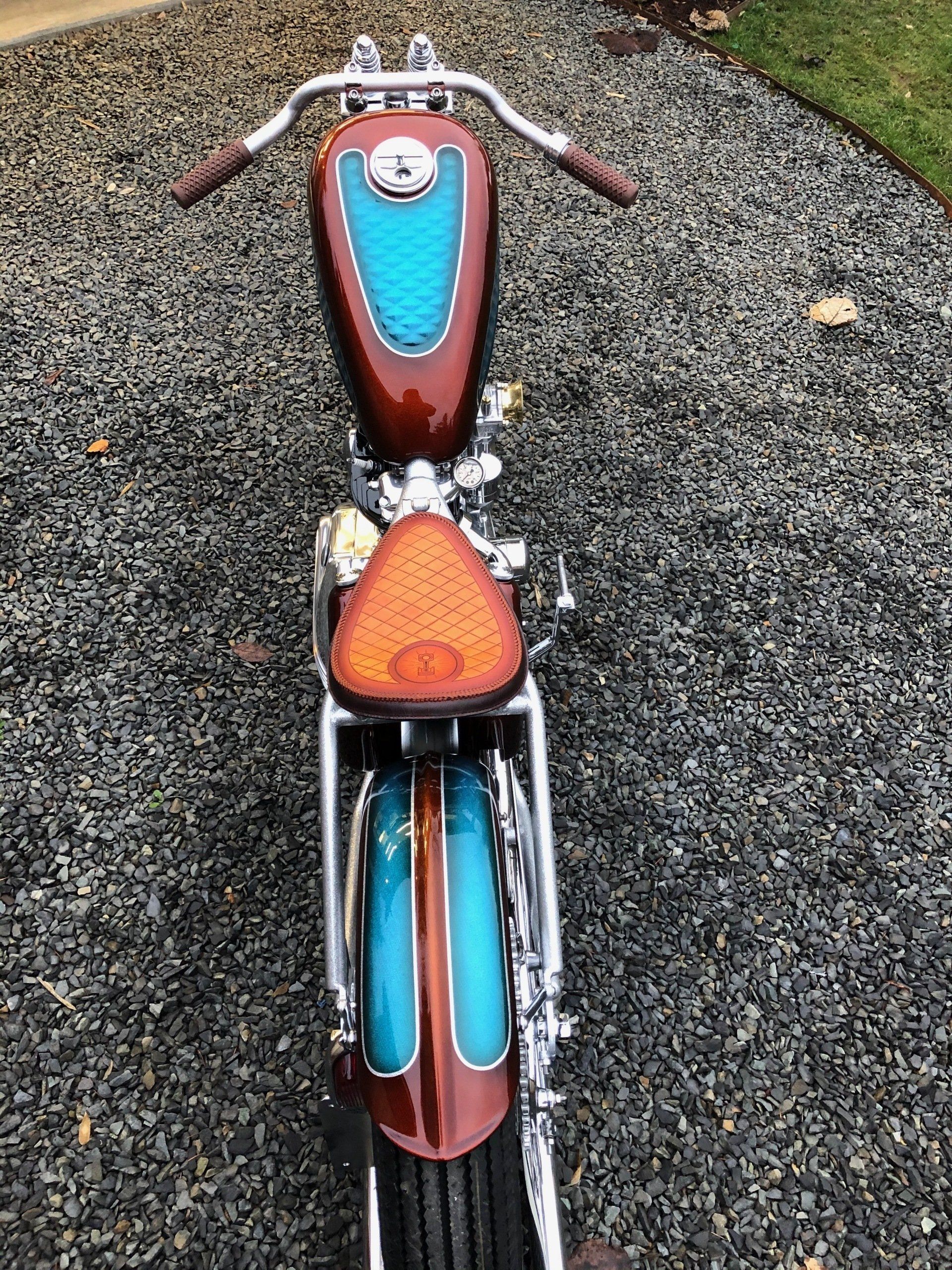 Top view of a red and turquoise custom motorcycle on gravel, with a triangular orange seat.