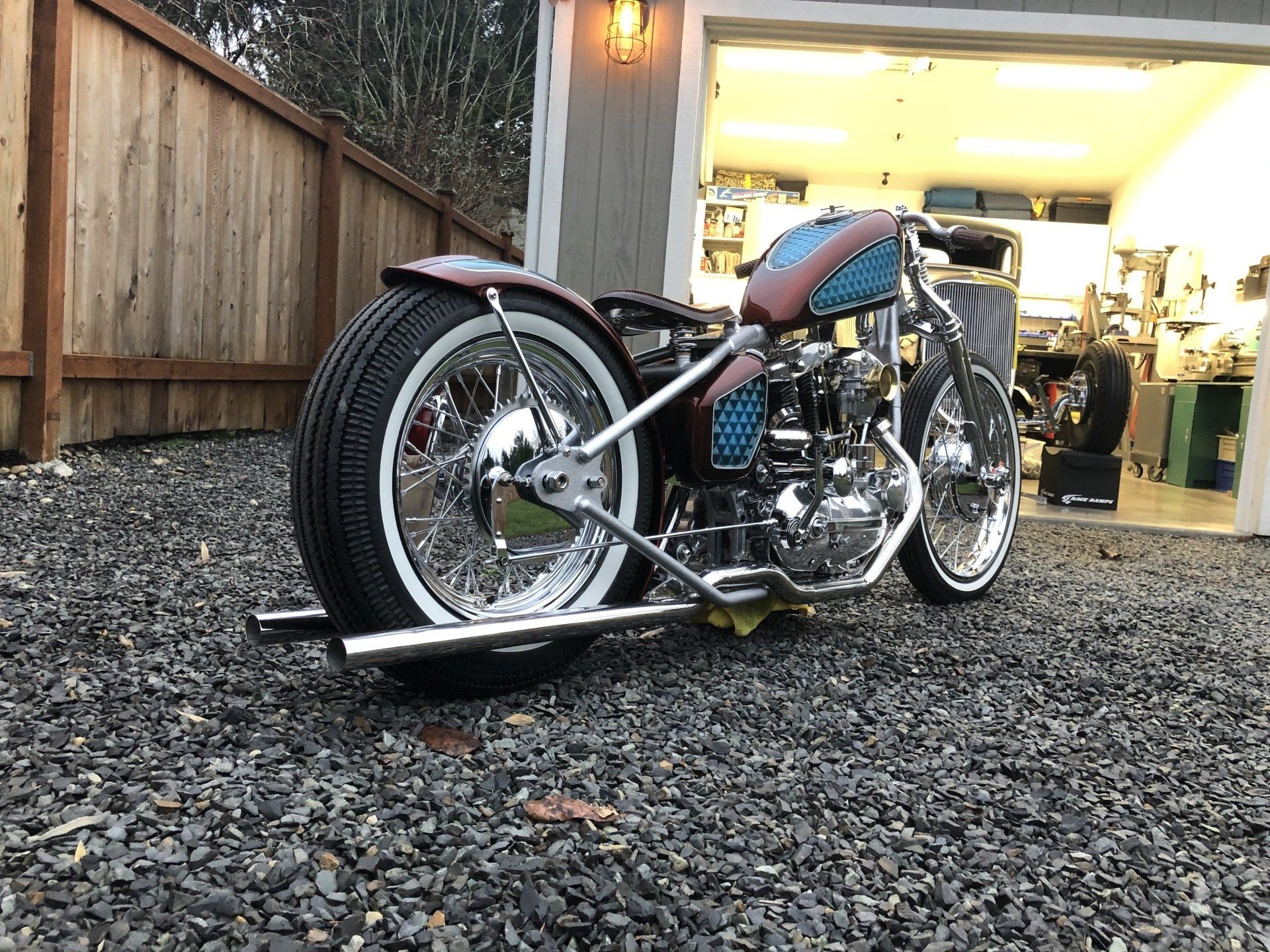 Custom motorcycle parked on gravel beside a garage at dusk