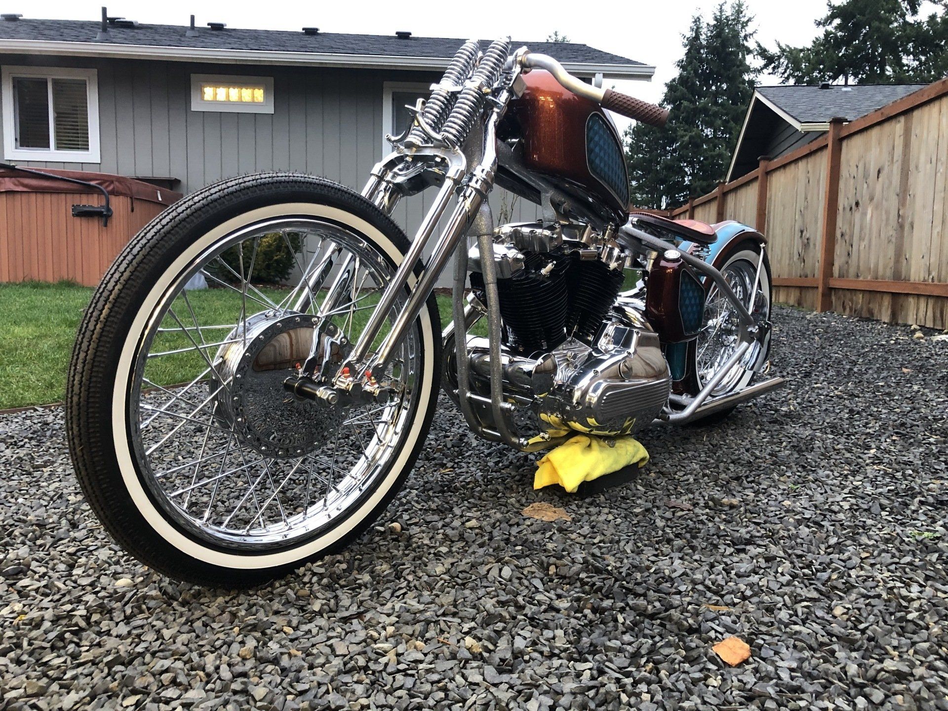 Custom black chopper motorcycle with chrome wheels parked on gravel in a residential yard