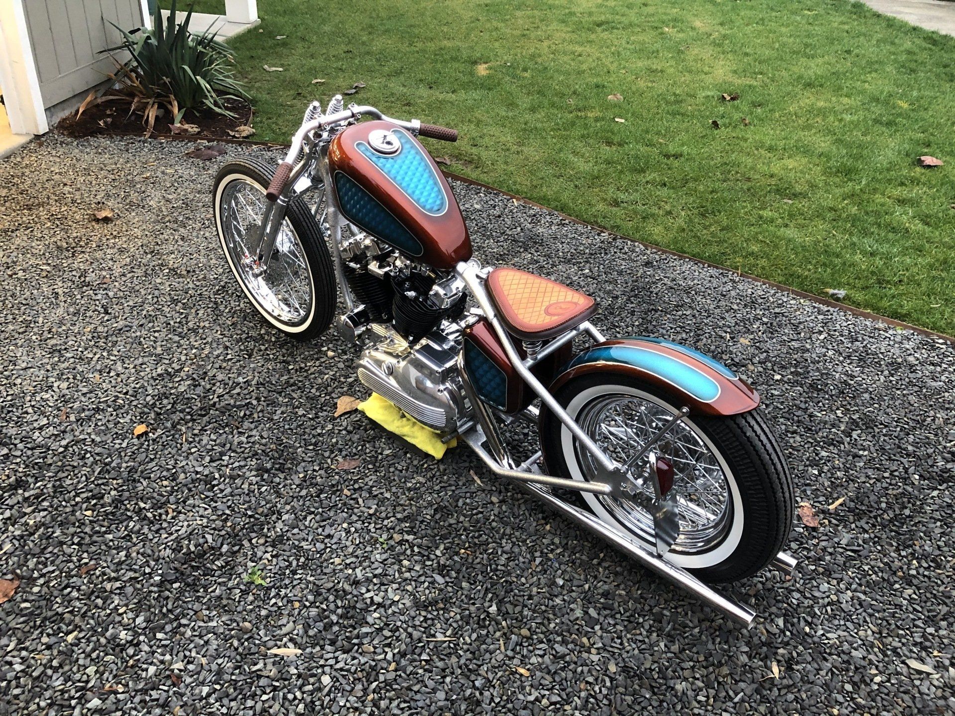 Custom red-and-blue motorcycle parked on gravel beside a lawn and house wall