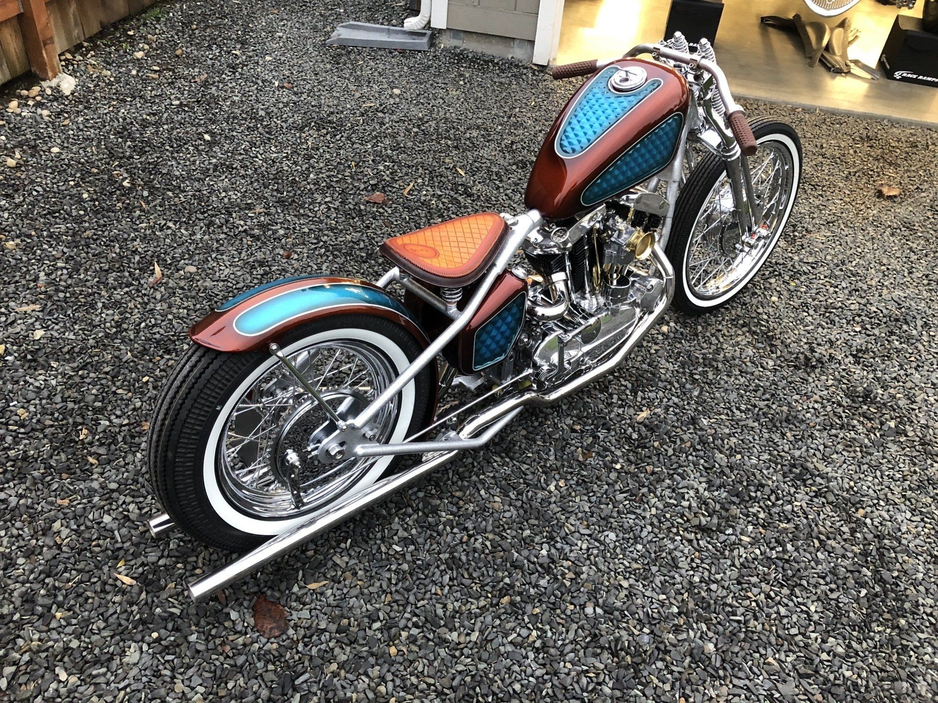 Custom blue and orange motorcycle with chrome details parked on gravel