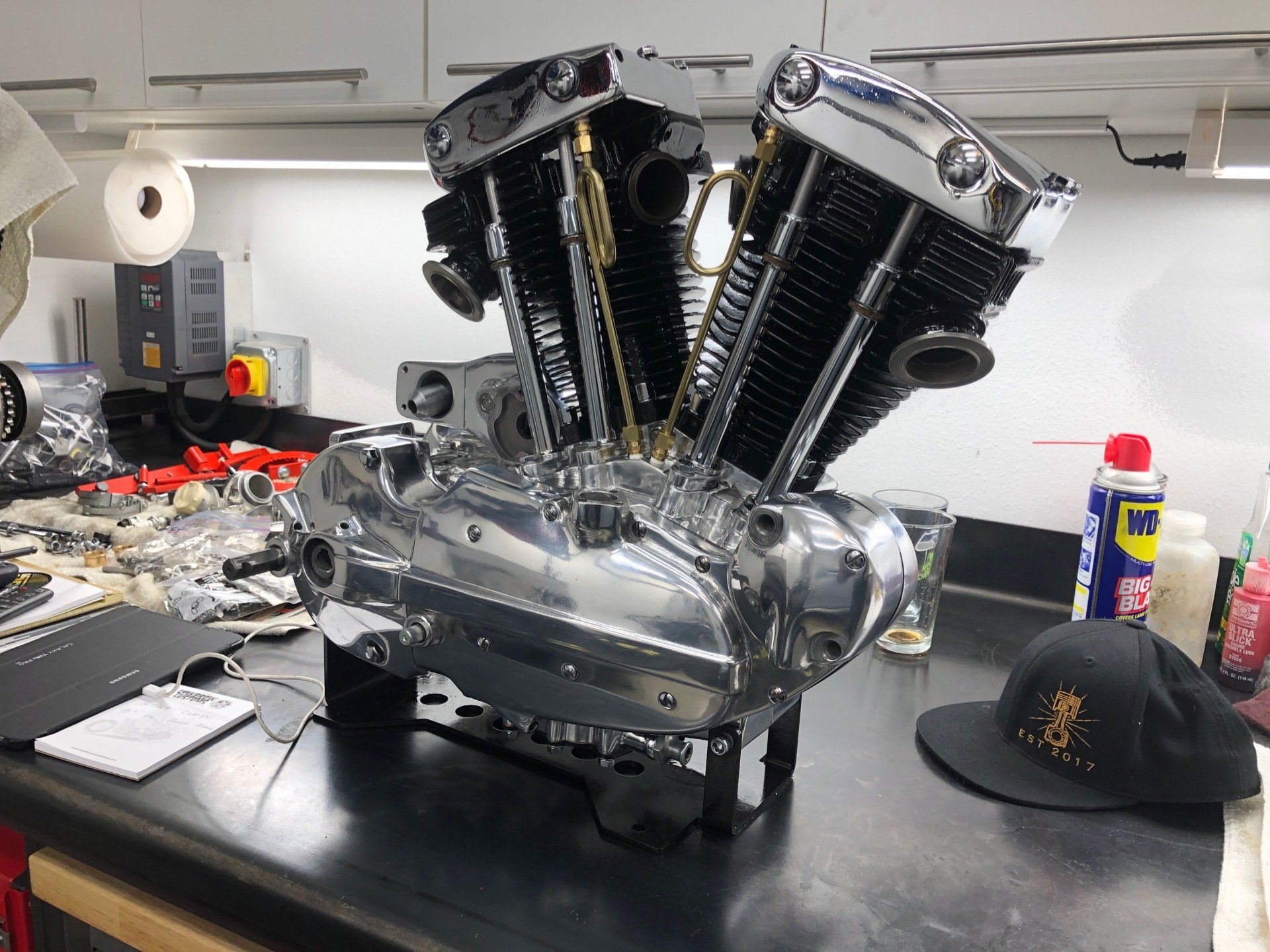 Custom V8 engine on a workbench in a garage, with tools, parts, and a black cap nearby
