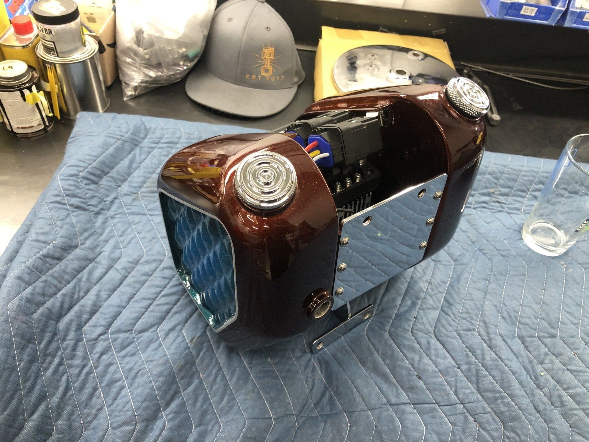 Brown bottle covered in leather on a quilted mat, with a helmet and small glass in the background