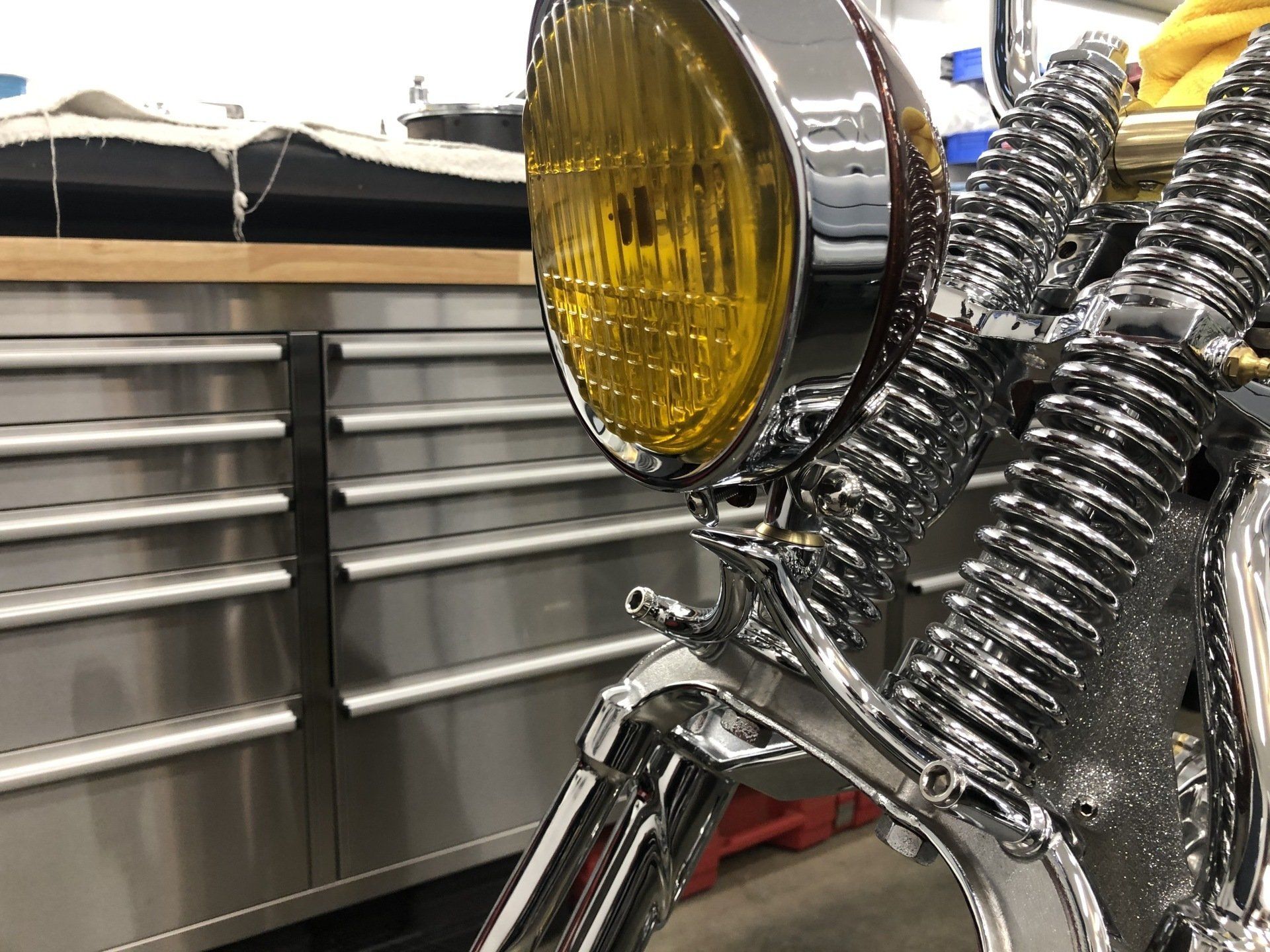 Chrome motorcycle front with yellow headlight and ribbed metal body in a garage background