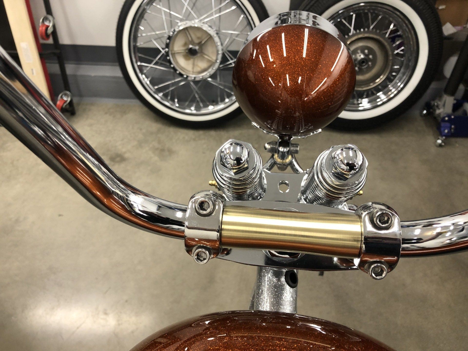 Chrome motorcycle handlebars with brown fuel tank and twin gauges in a garage