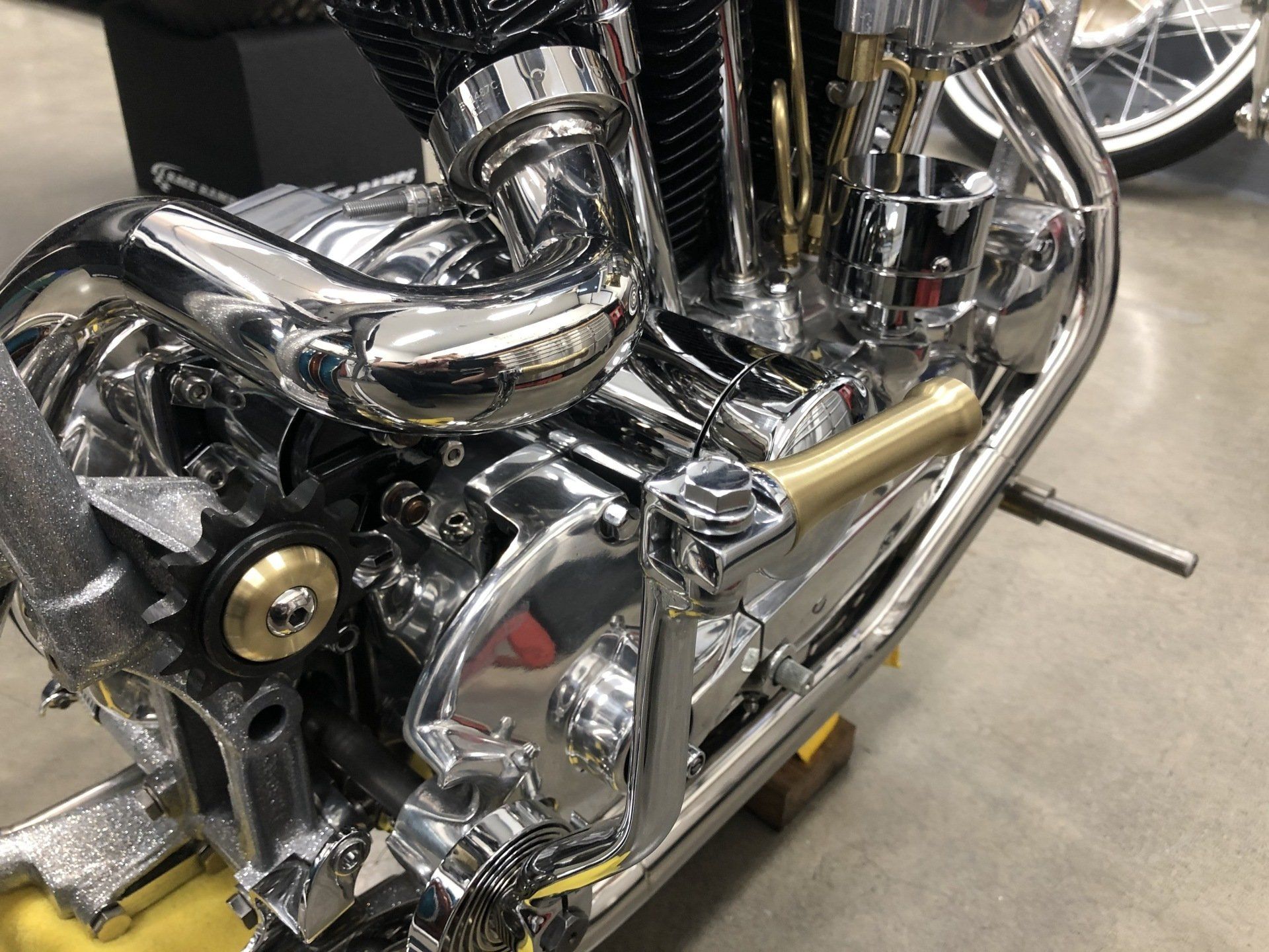 Close-up of a chrome motorcycle engine and exhaust pipes in a workshop or garage.