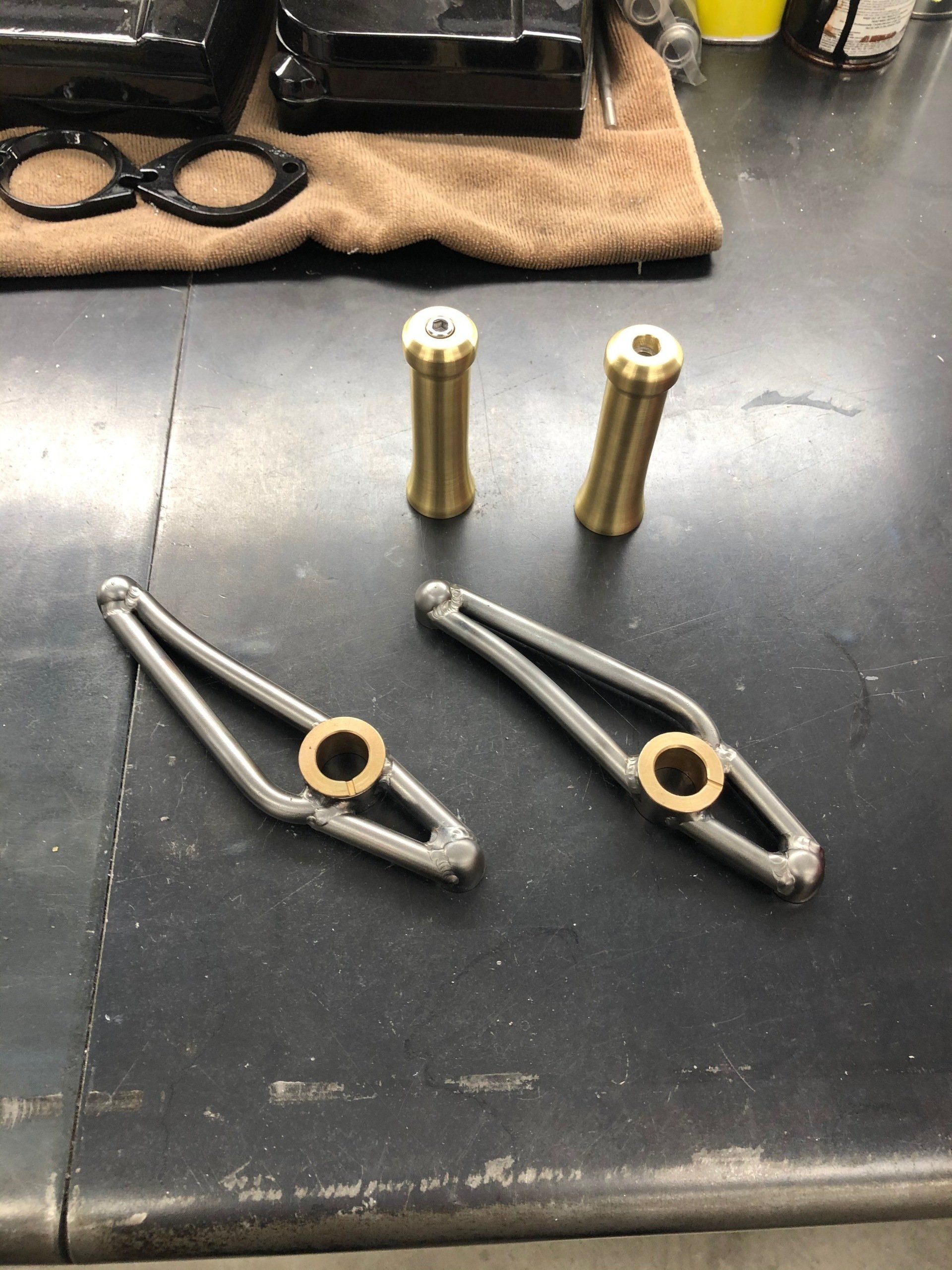 Two brass cylinders and two silver linkage arms on a dark workbench.