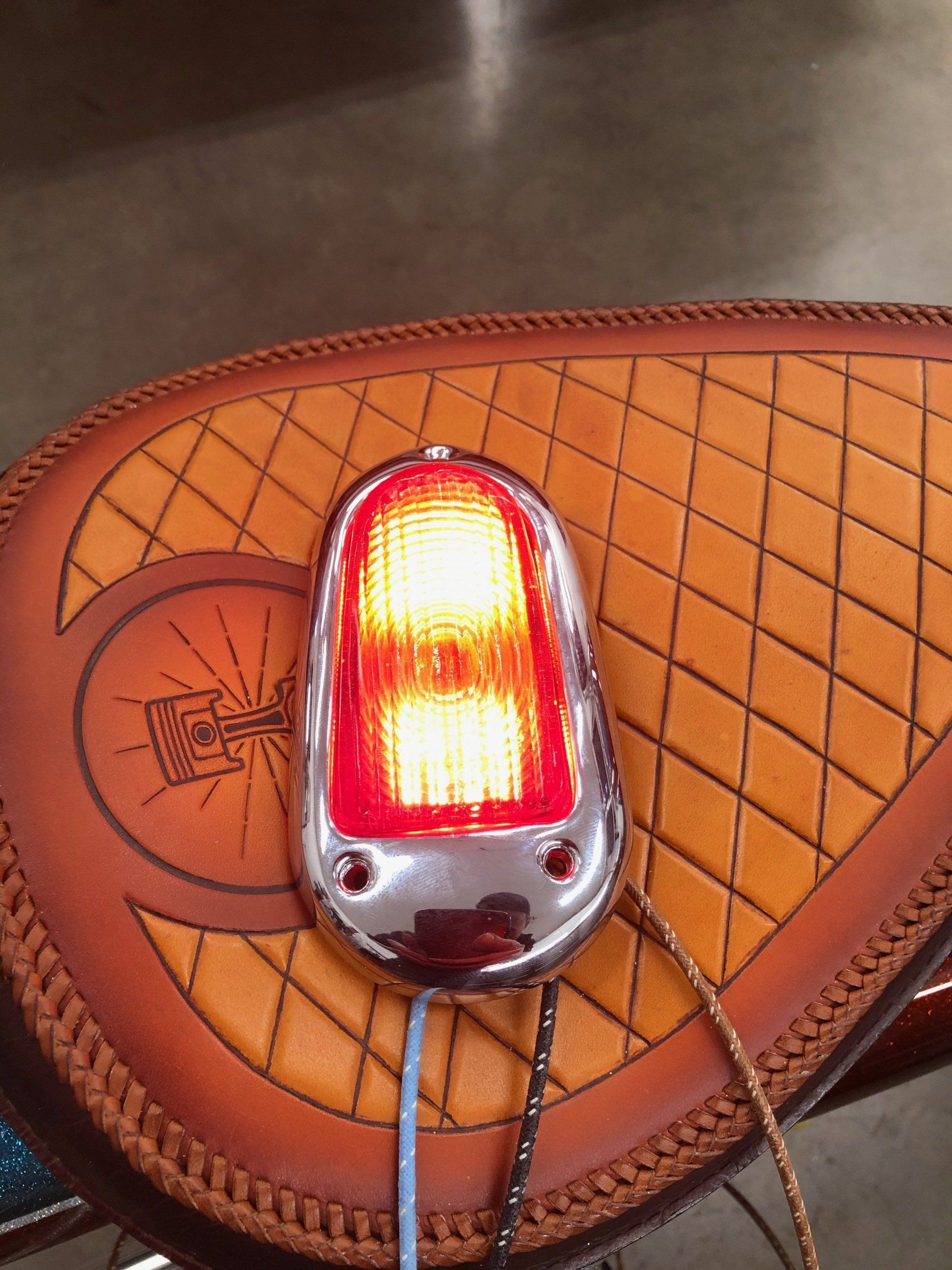 Glowing red tail light resting on a brown leather motorcycle seat with stitched trim