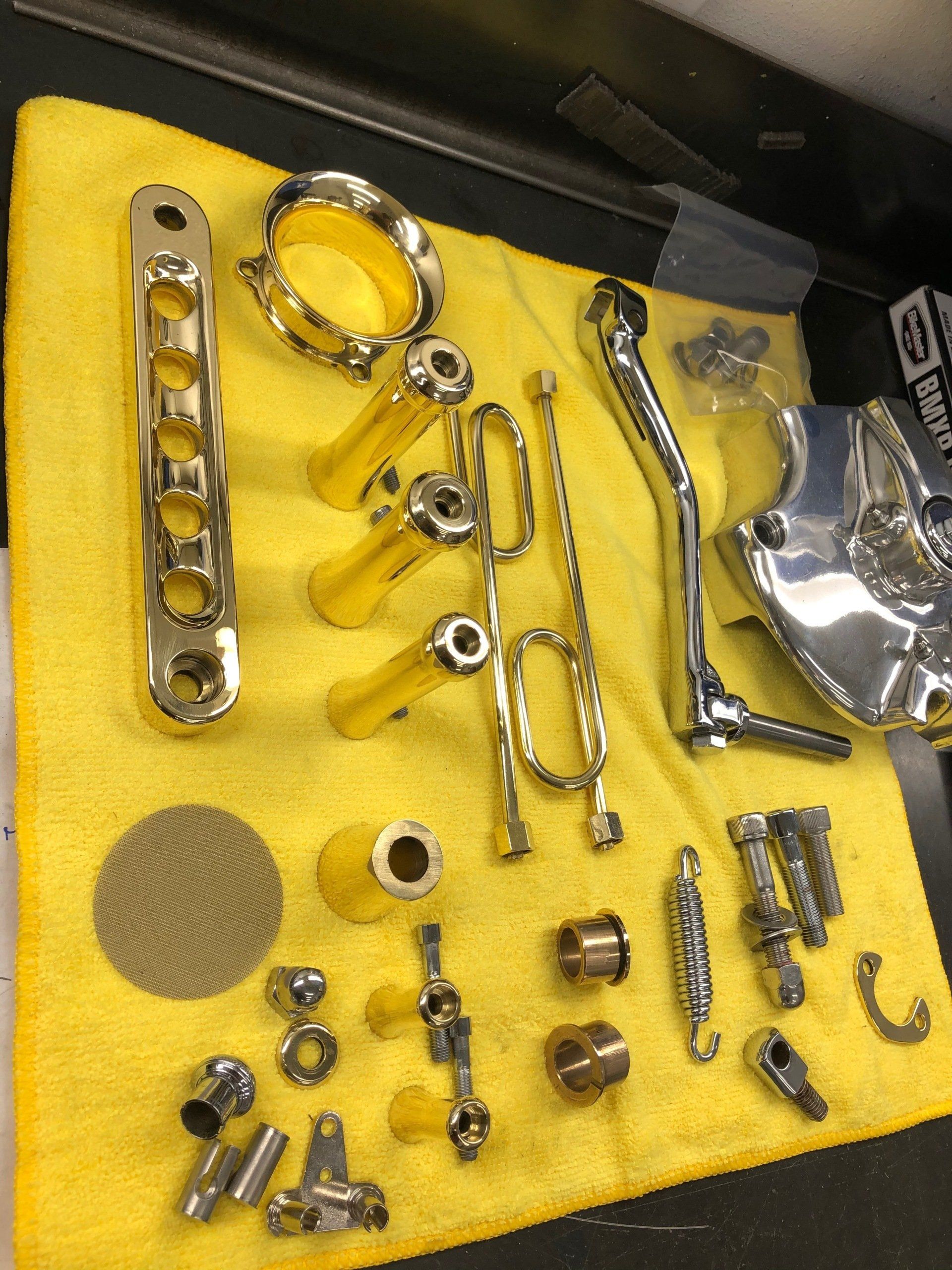 Assorted metal automotive parts laid out on a yellow cloth, including rings, brackets, bolts, and fittings.