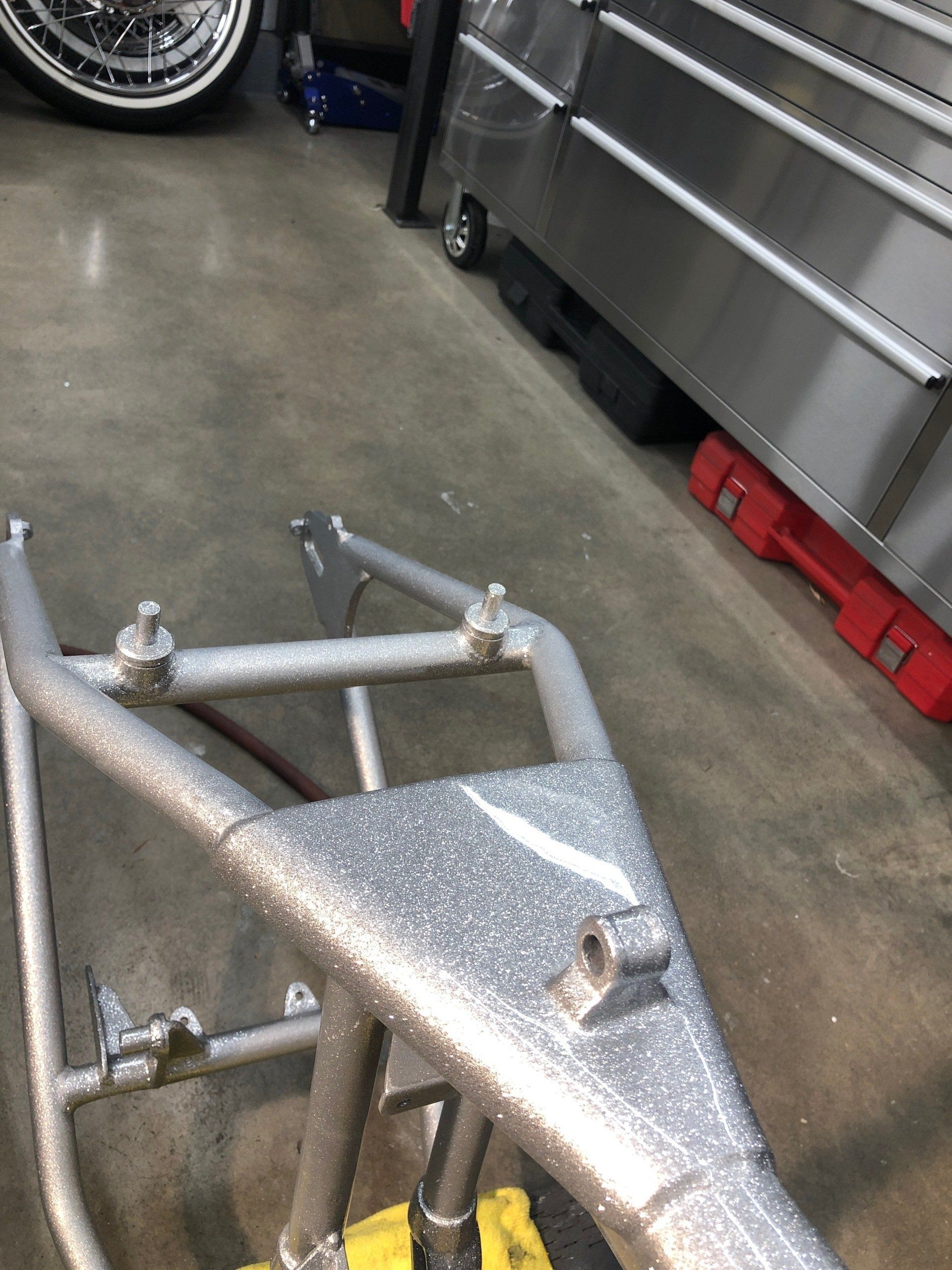 Silver metal bike frame in a workshop garage beside a tool chest and wheel