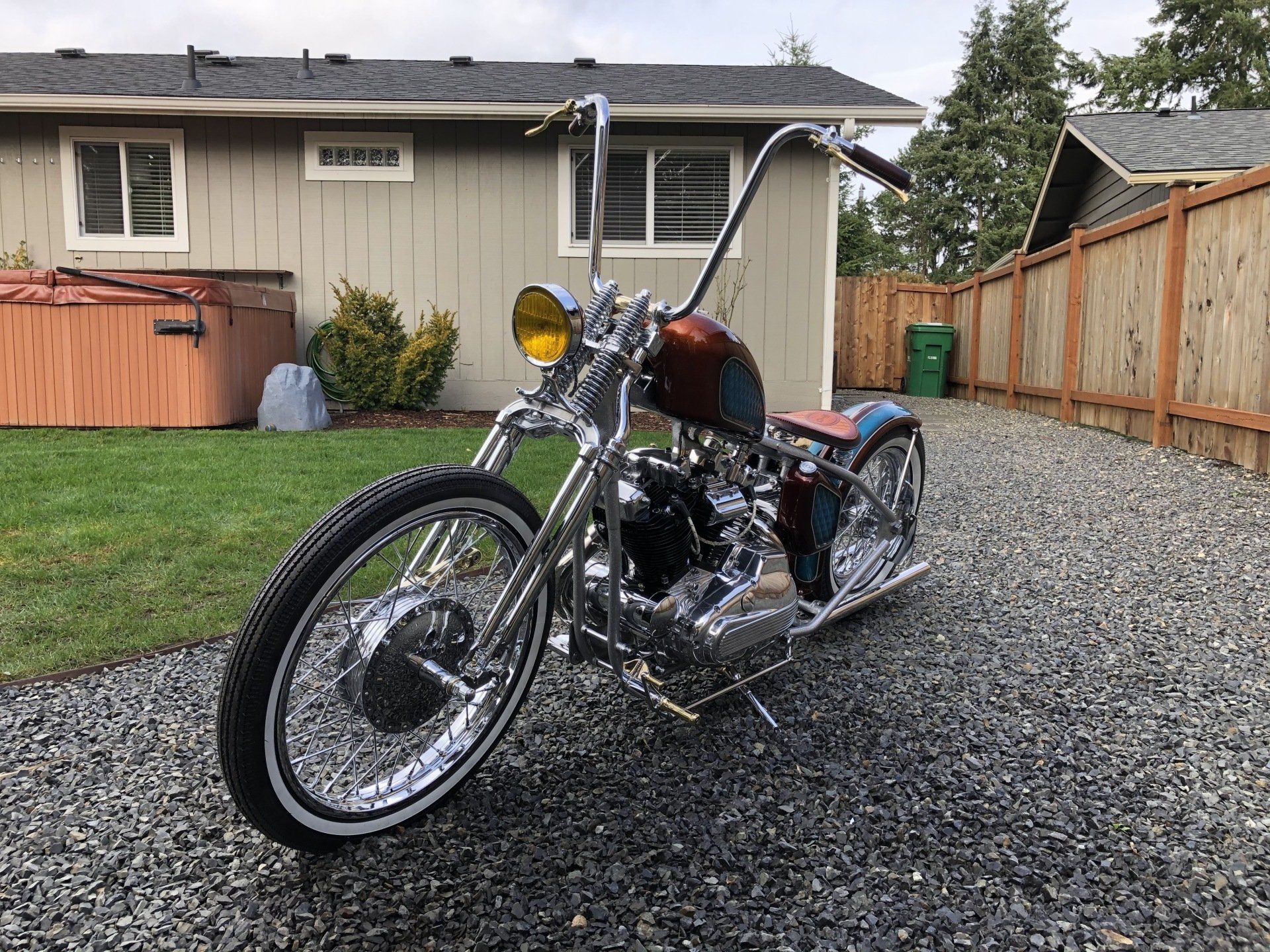 Chrome motorcycle parked on gravel in front of a beige house and wooden fence.