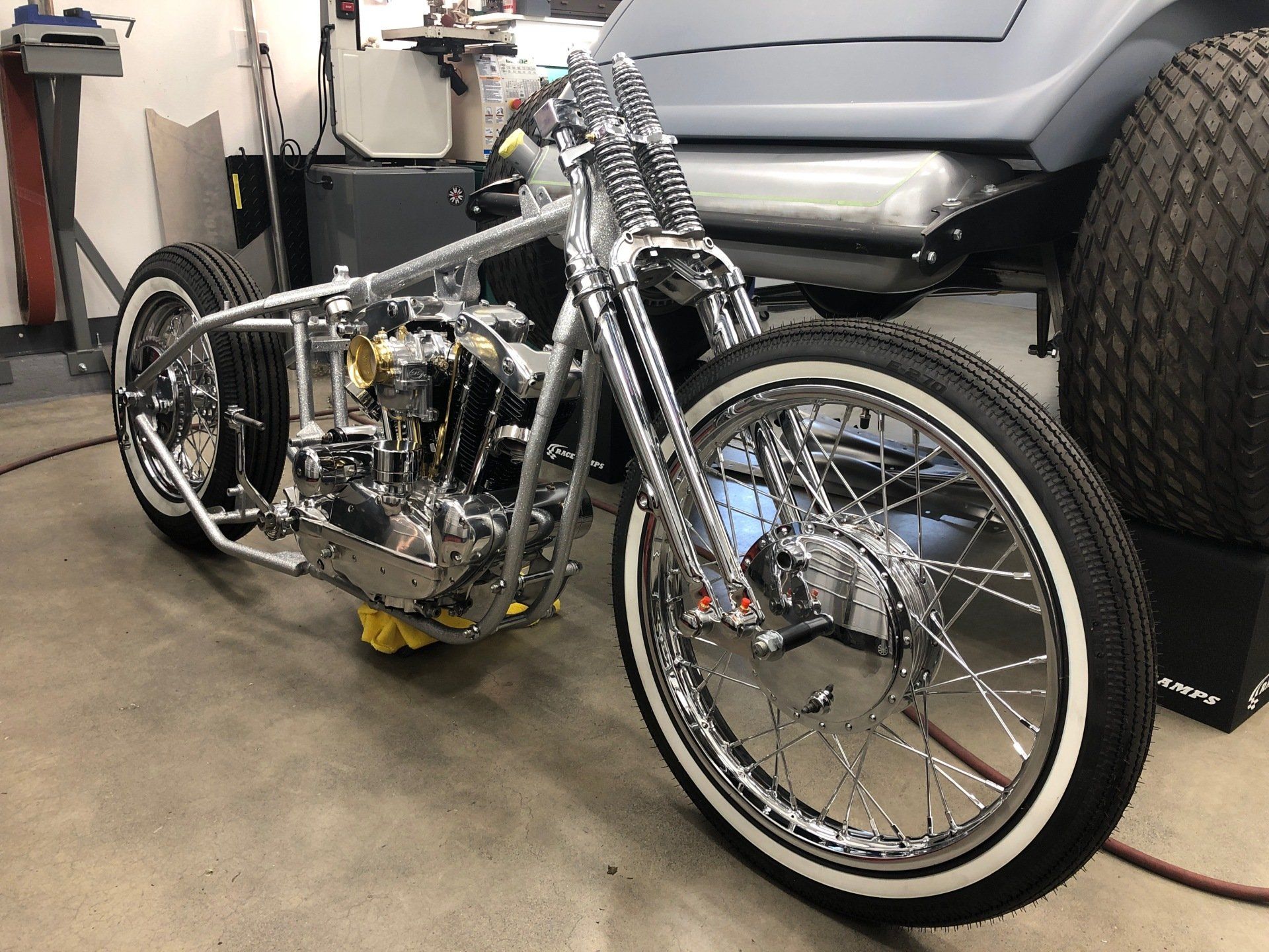 Custom chrome motorcycle in a garage, with a large rear tire and shiny front wheel.