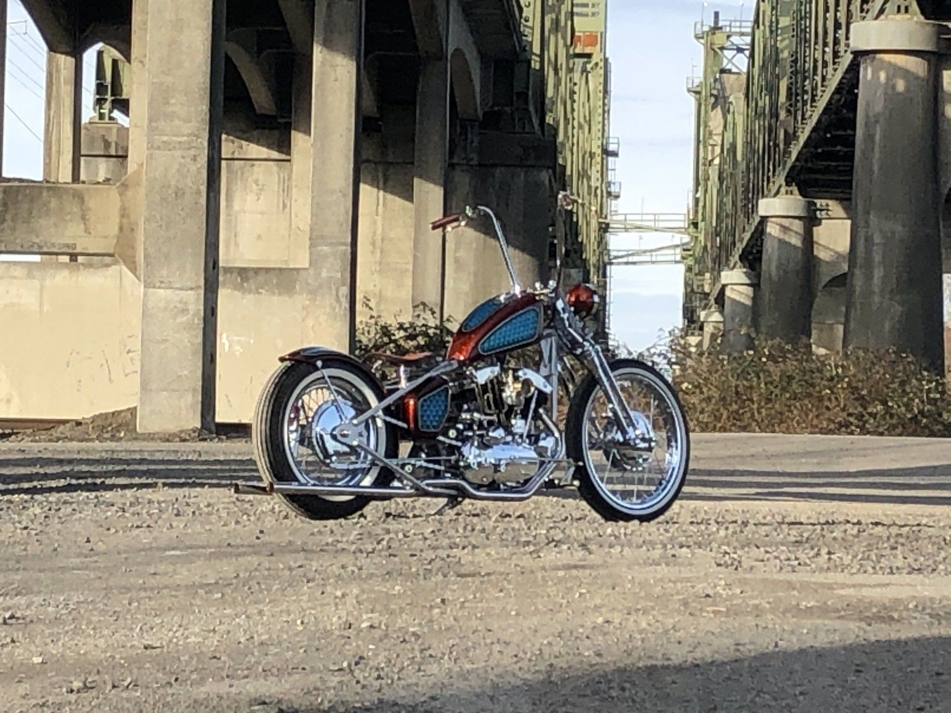 Custom chopper motorcycle parked under a bridge in an industrial area