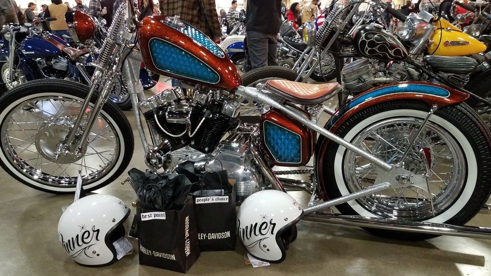 Custom blue-and-red motorcycle on display with white helmets and black bags in front