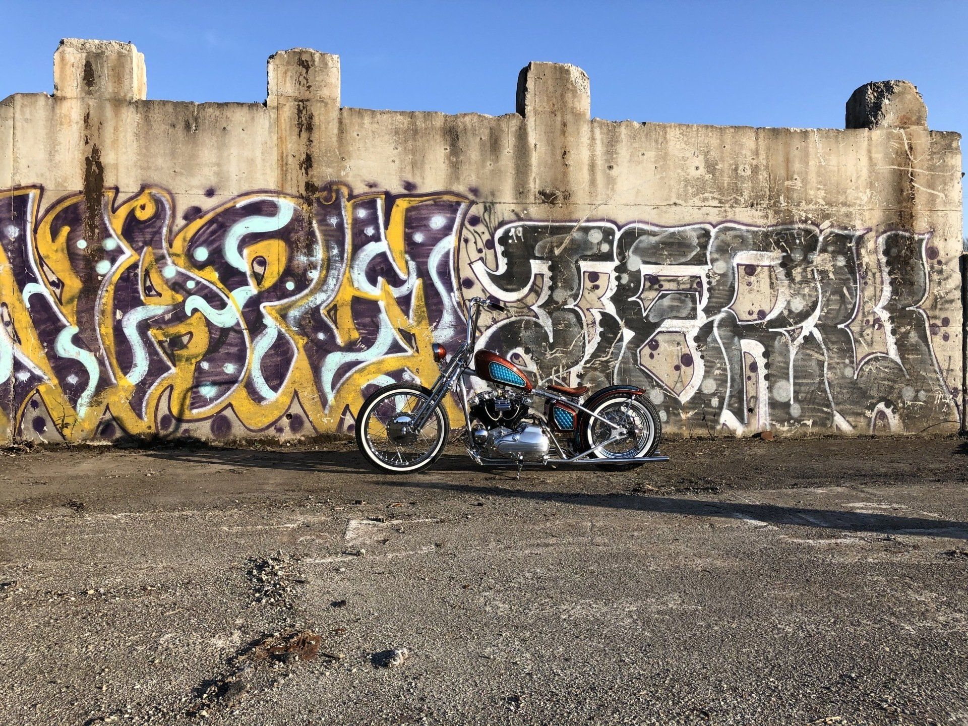 Motorcycle parked in front of a graffiti-covered concrete wall under a clear blue sky