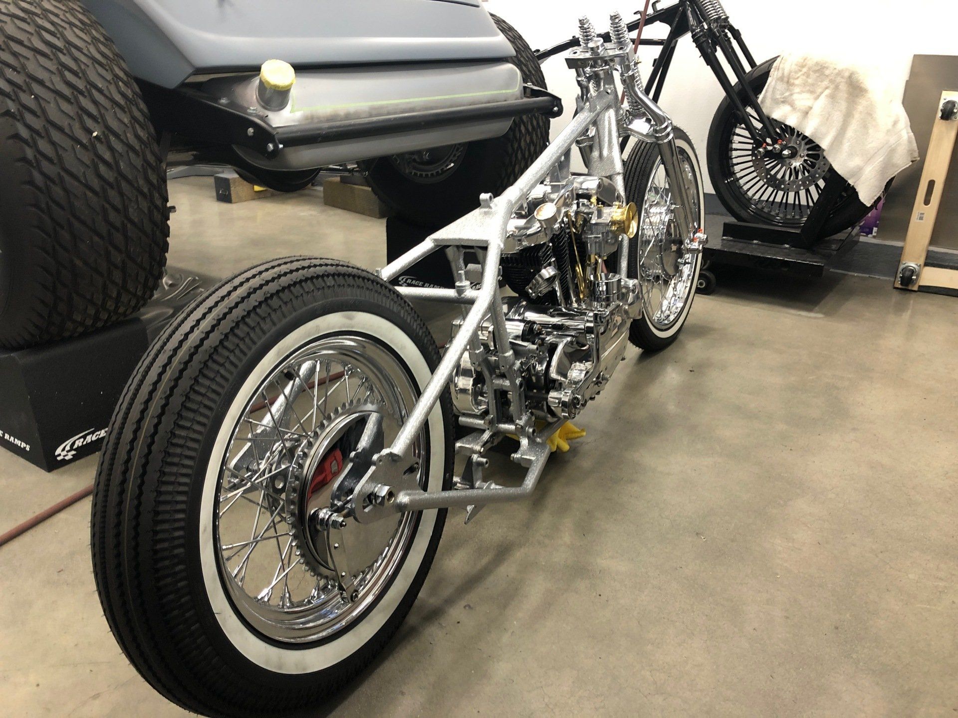 Custom chrome chopper motorcycle in a garage, viewed from the rear-left side.